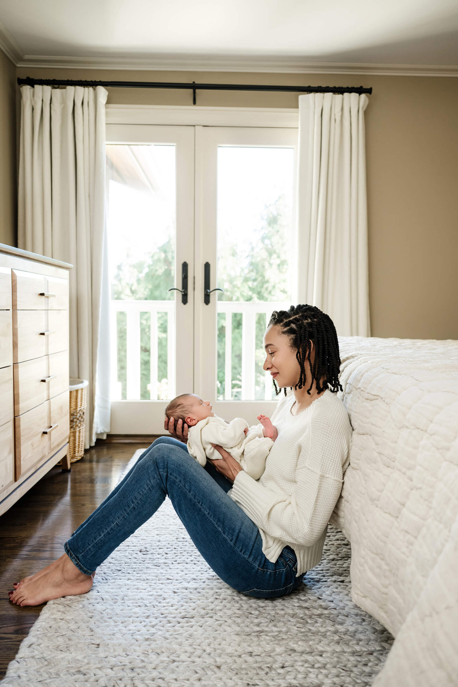 Mother sitting on the bedroom floor and holding her newborn baby during a relaxed in-home newborn session.
