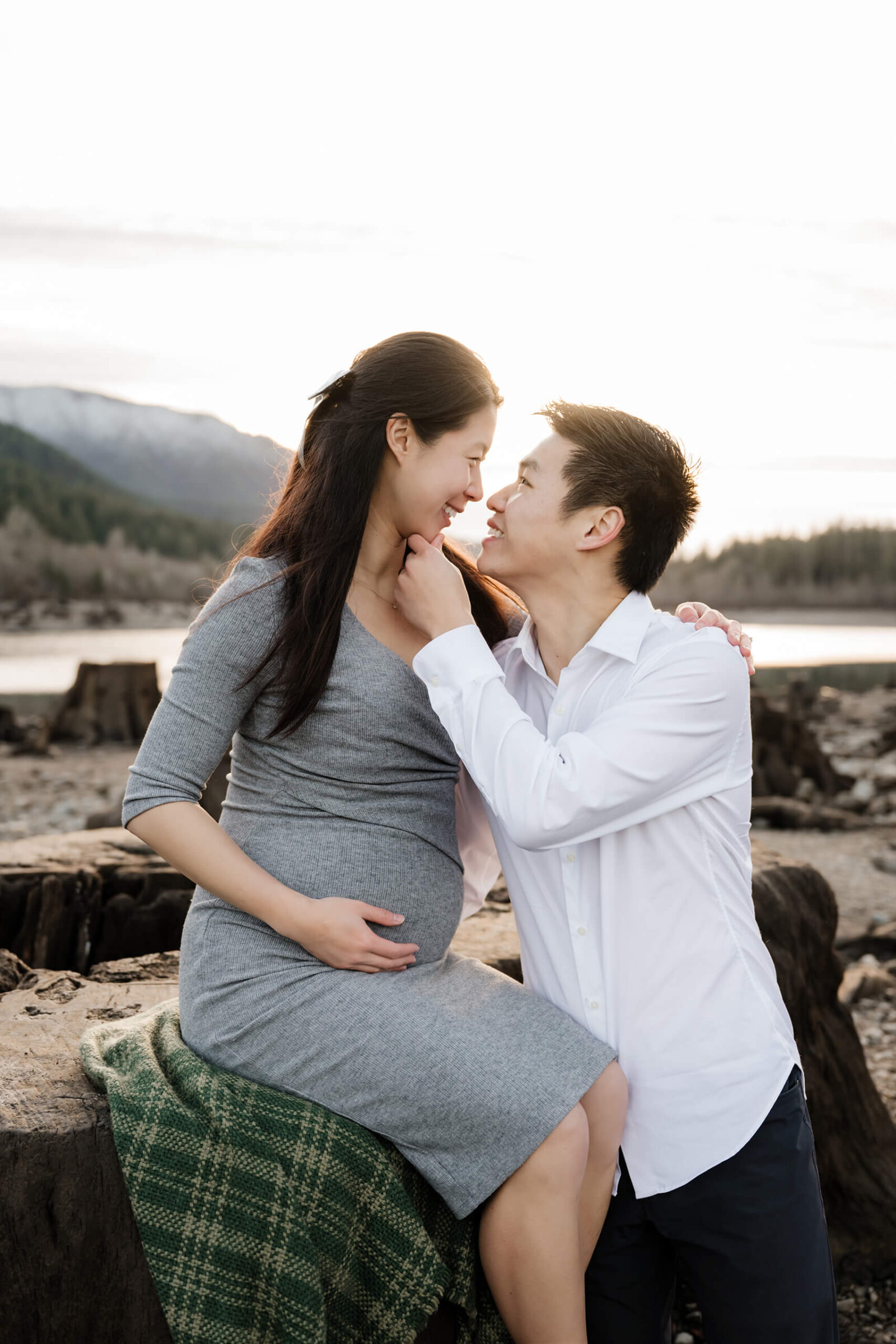 Expecting parents smiling together during an outdoor maternity session by the lake.