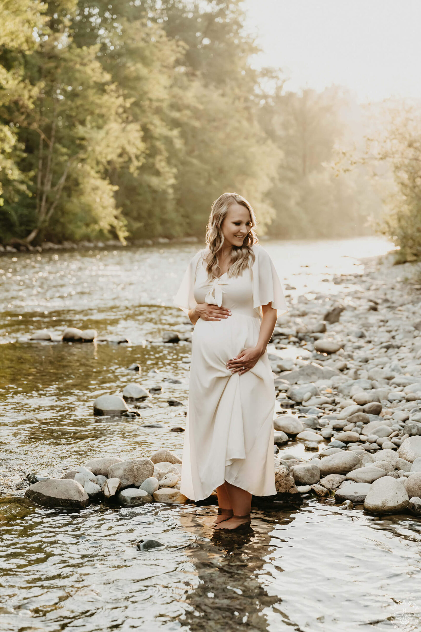 Expecting mother standing in a shallow river during a golden hour outdoor maternity session.