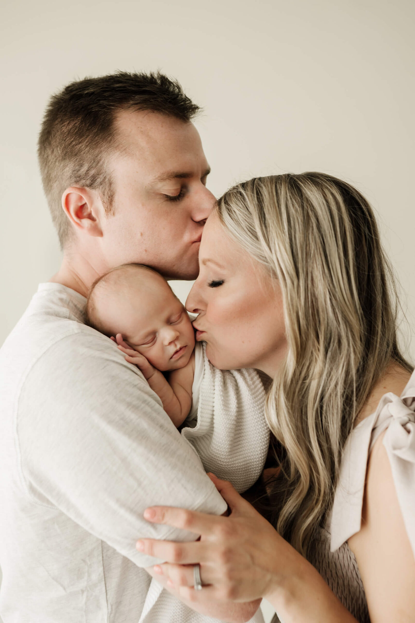 Parents kissing their newborn baby during a soft natural newborn family portrait.