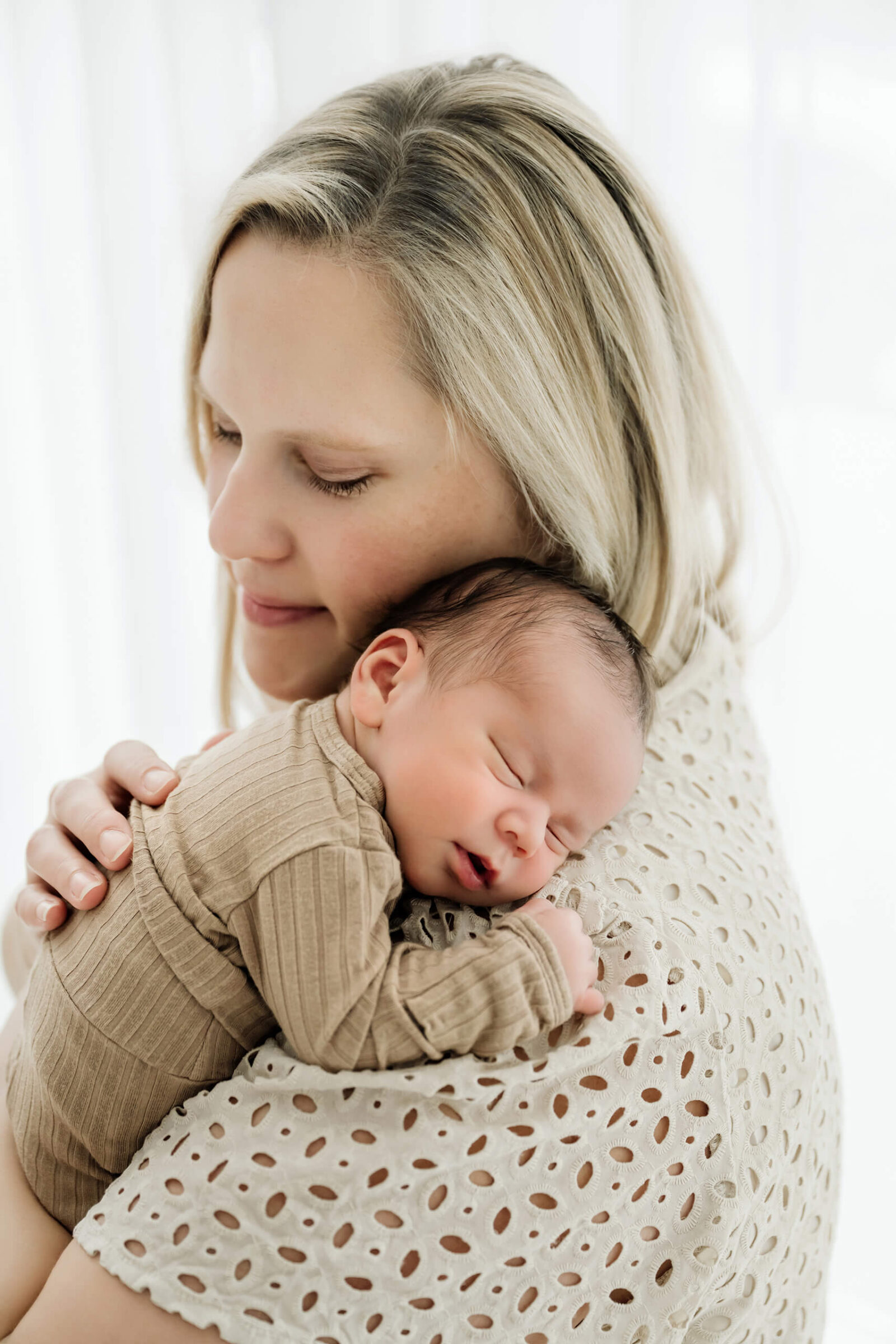 Mother holding her sleeping newborn baby close during a soft natural newborn portrait.