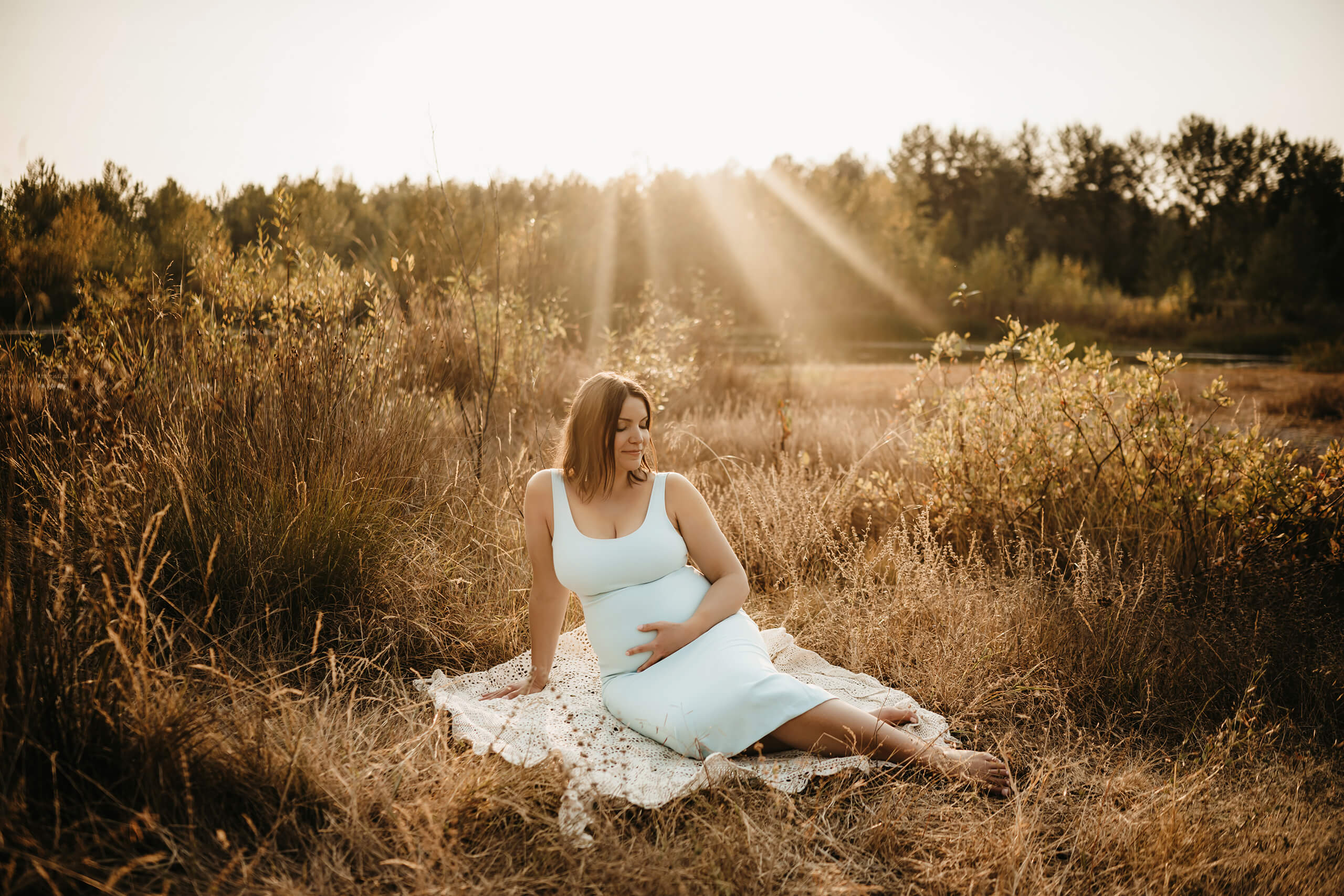 Expecting mom in a white dress sitting in golden grass during a warm outdoor maternity session in Redmond.