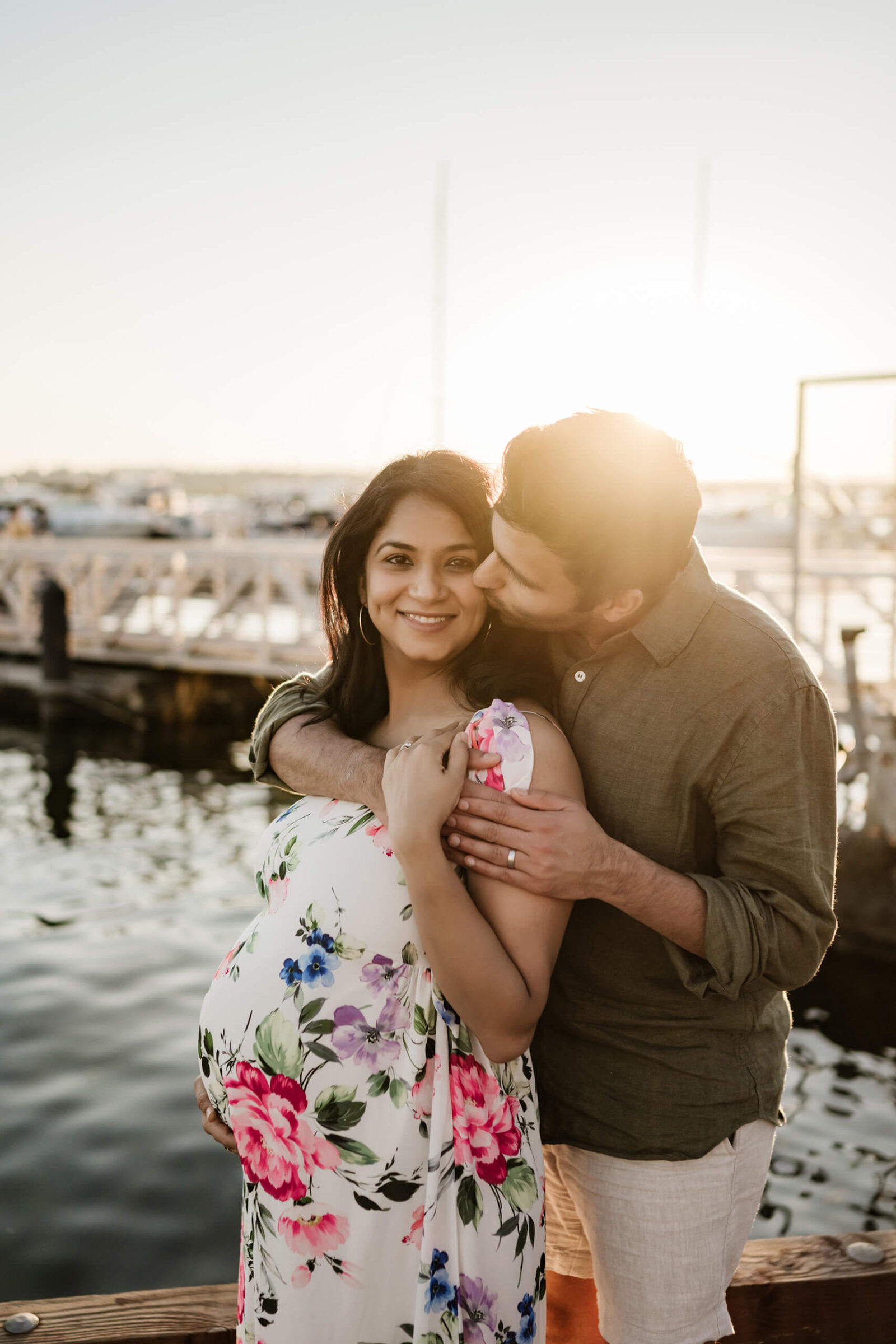 Expecting parents cuddling by the water during a golden-hour outdoor maternity session in Kirkland.
