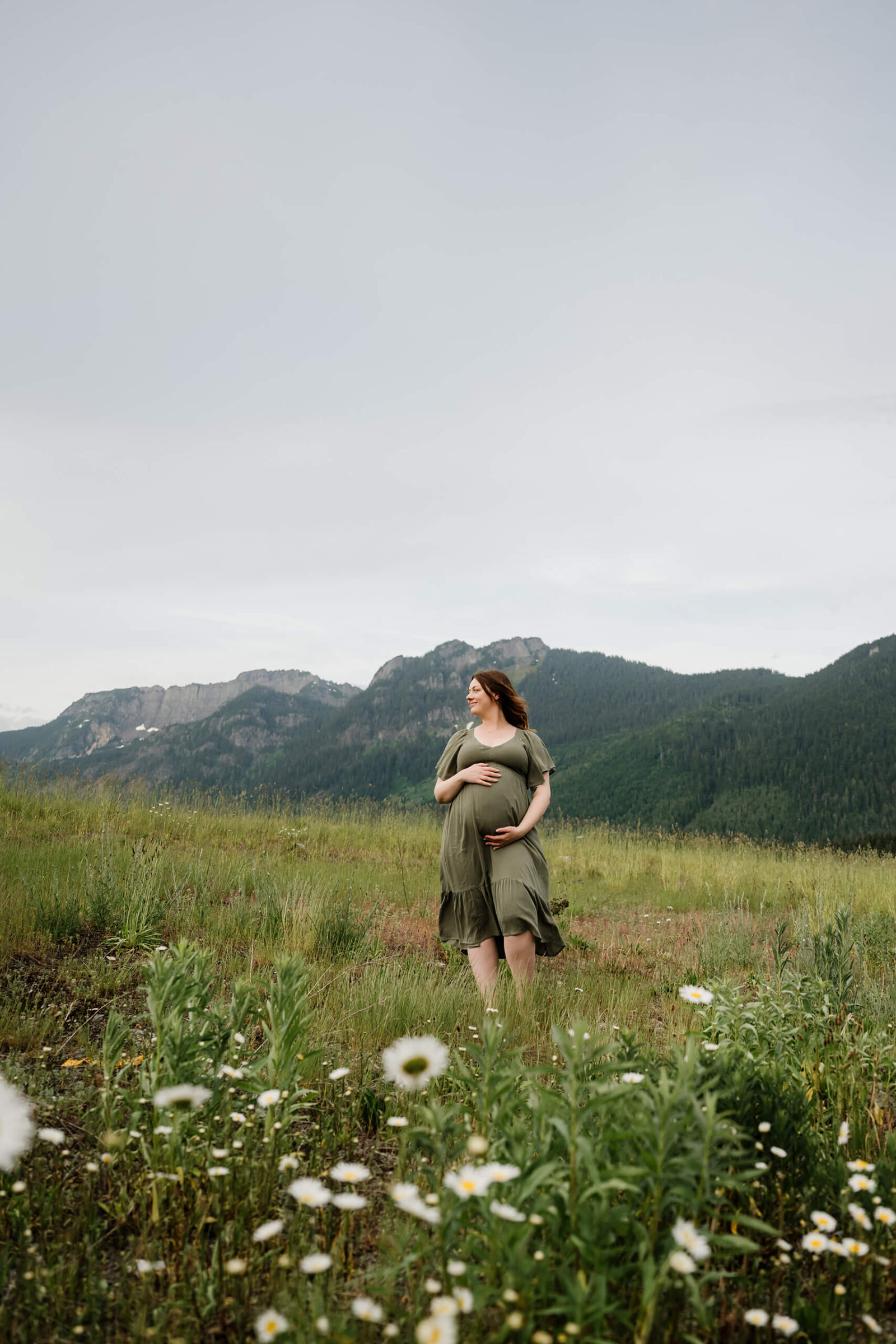 Expecting mom holding her baby bump in a mountain meadow during a scenic outdoor maternity session at Snoqualmie Pass.