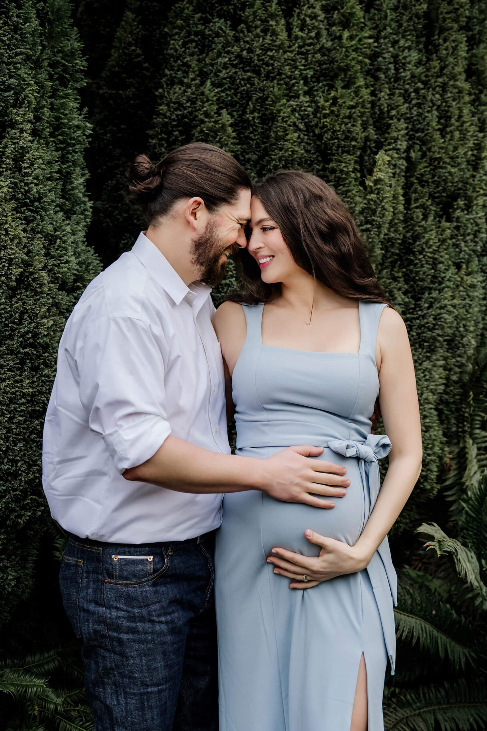 Expecting parents smiling together in a garden setting during a natural outdoor maternity session at WA Park Arboretum.