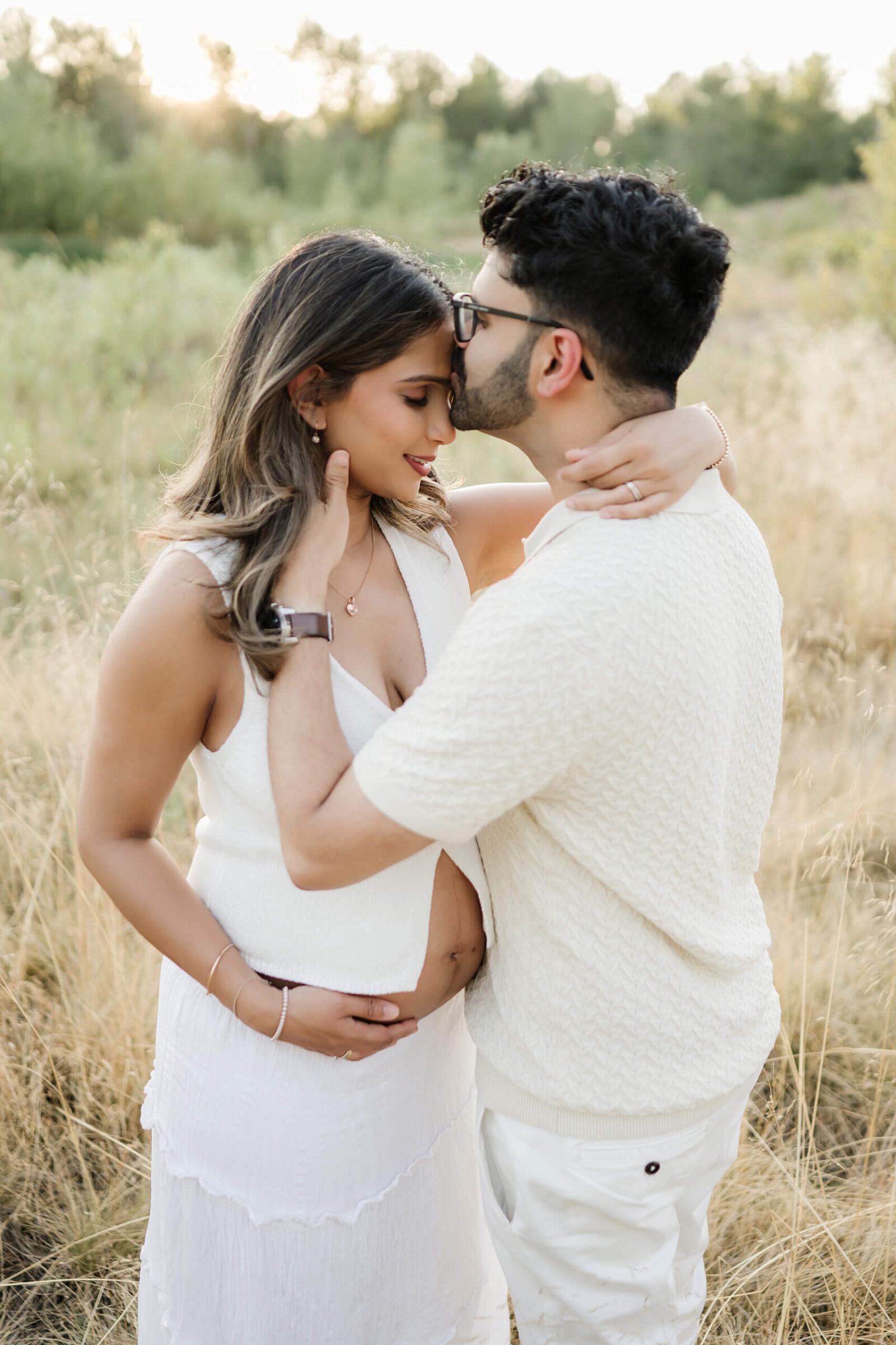 Expecting parents cuddling in a sunlit field during a soft outdoor maternity session in Redmond.