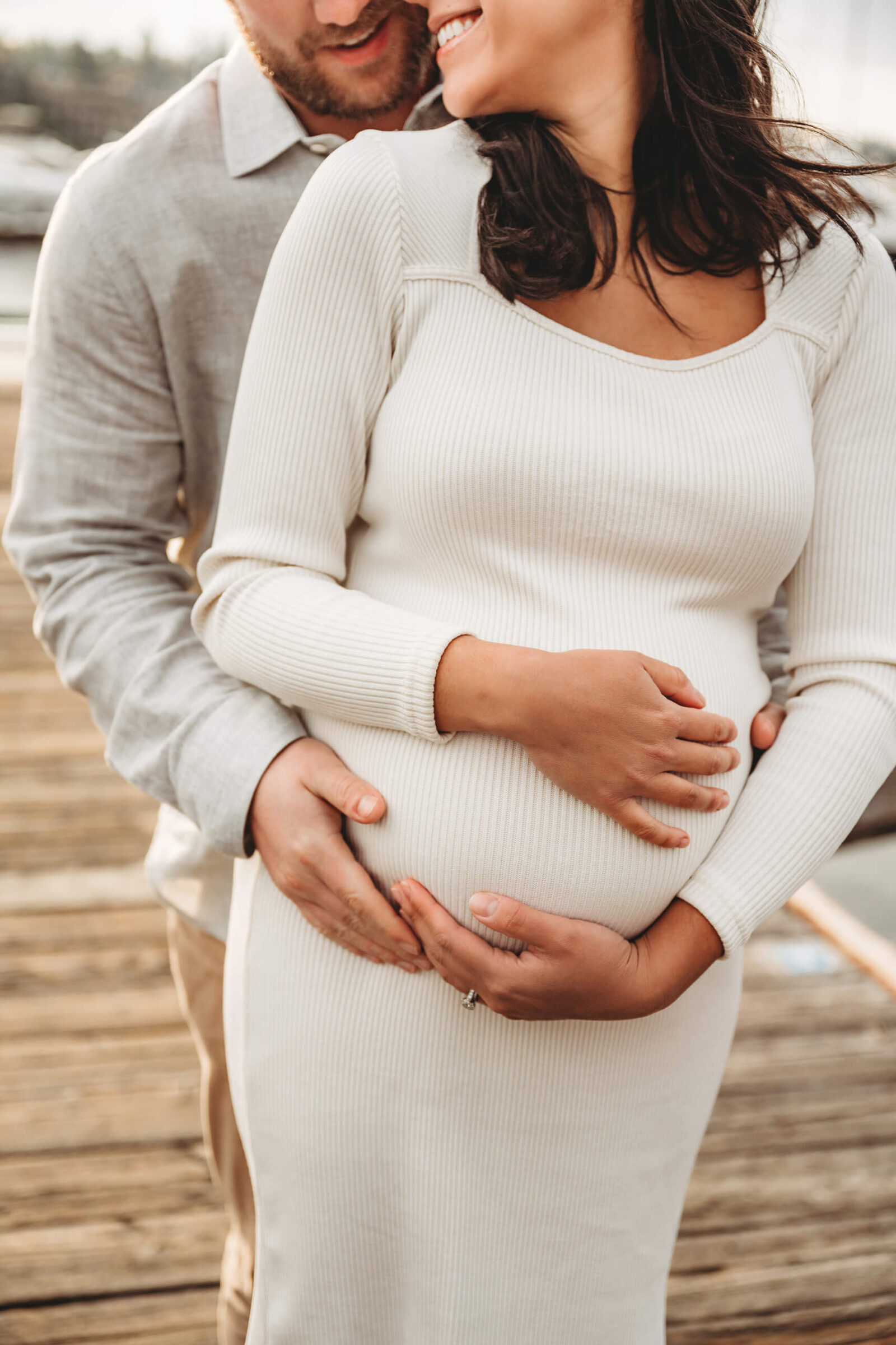 Close-up of expecting parents holding a baby bump during a natural outdoor maternity session in Kirkland Marina.