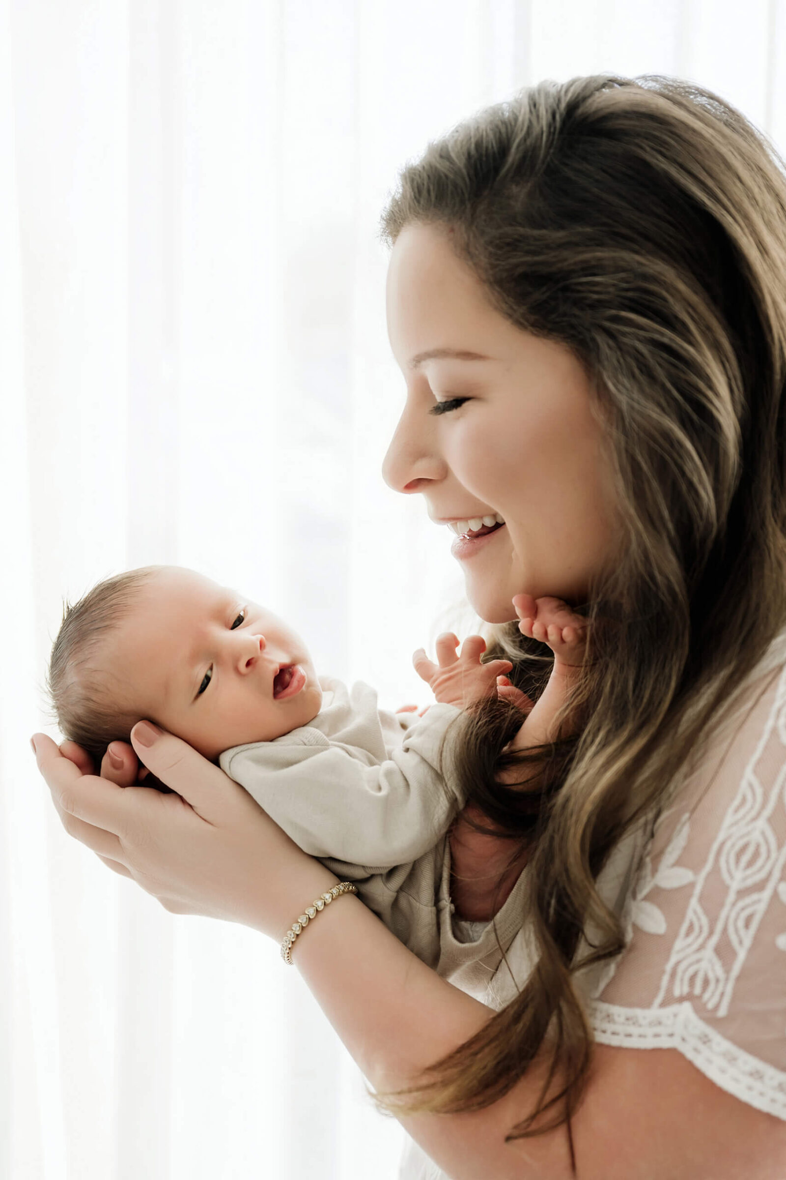 Mom smiling at her newborn baby during a soft studio newborn session, part of a maternity and newborn photography package.