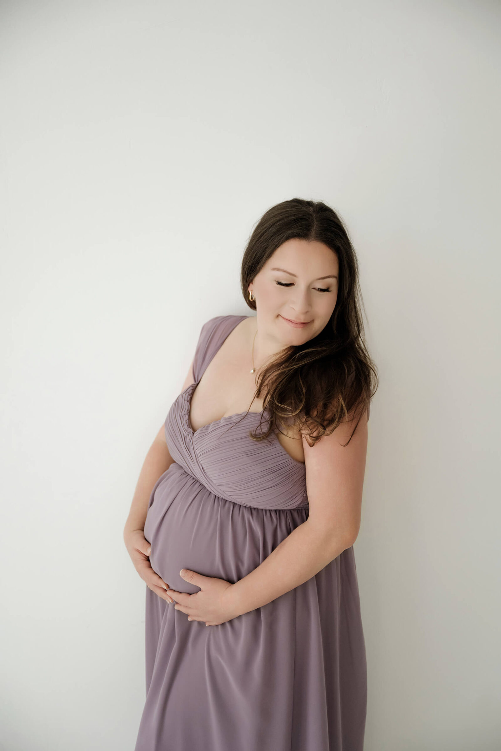 Expecting mom in a mauve dress gently holding her belly during a natural studio maternity session.
