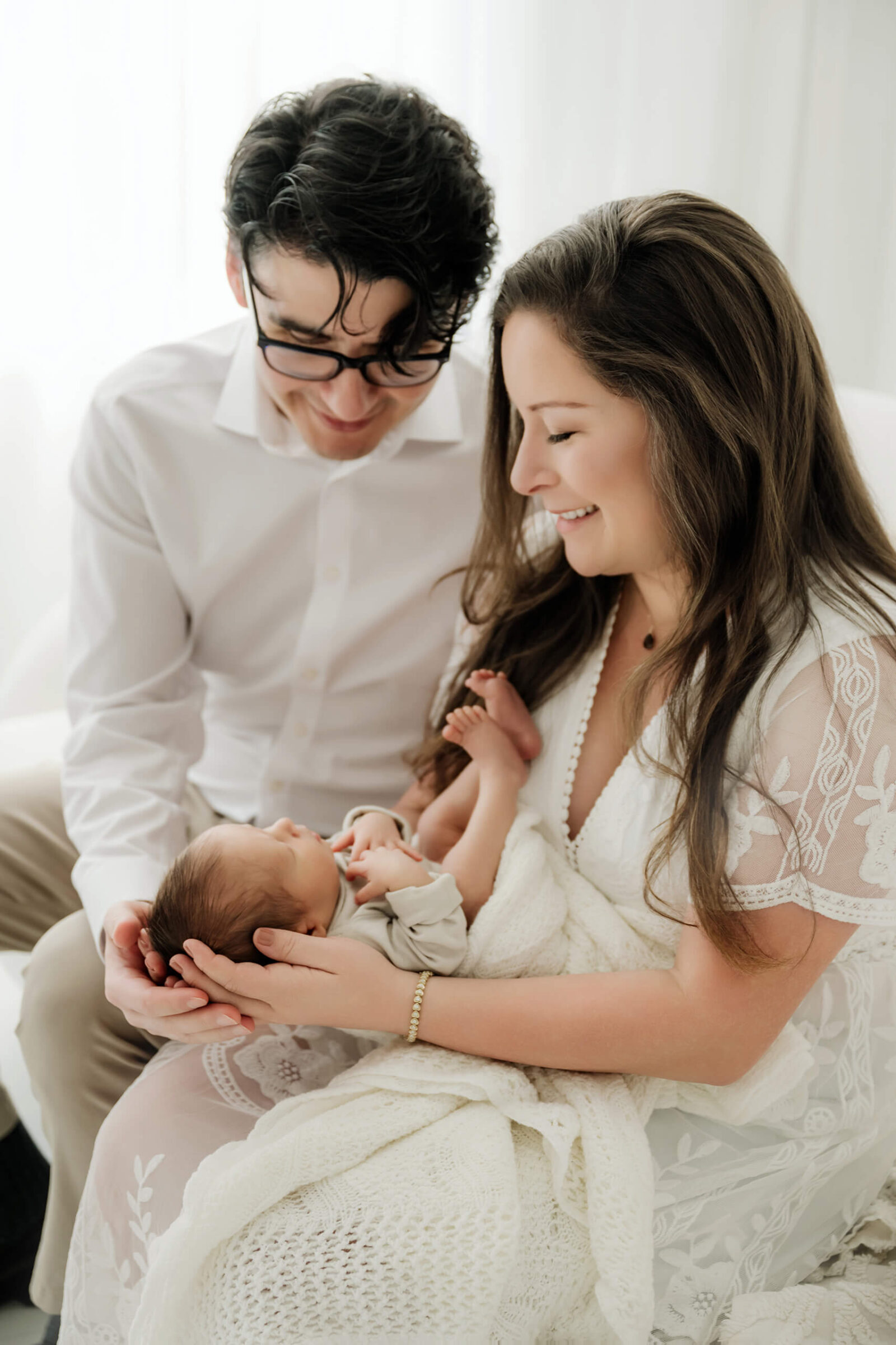 New parents sitting together with their newborn baby during a calm studio newborn session.