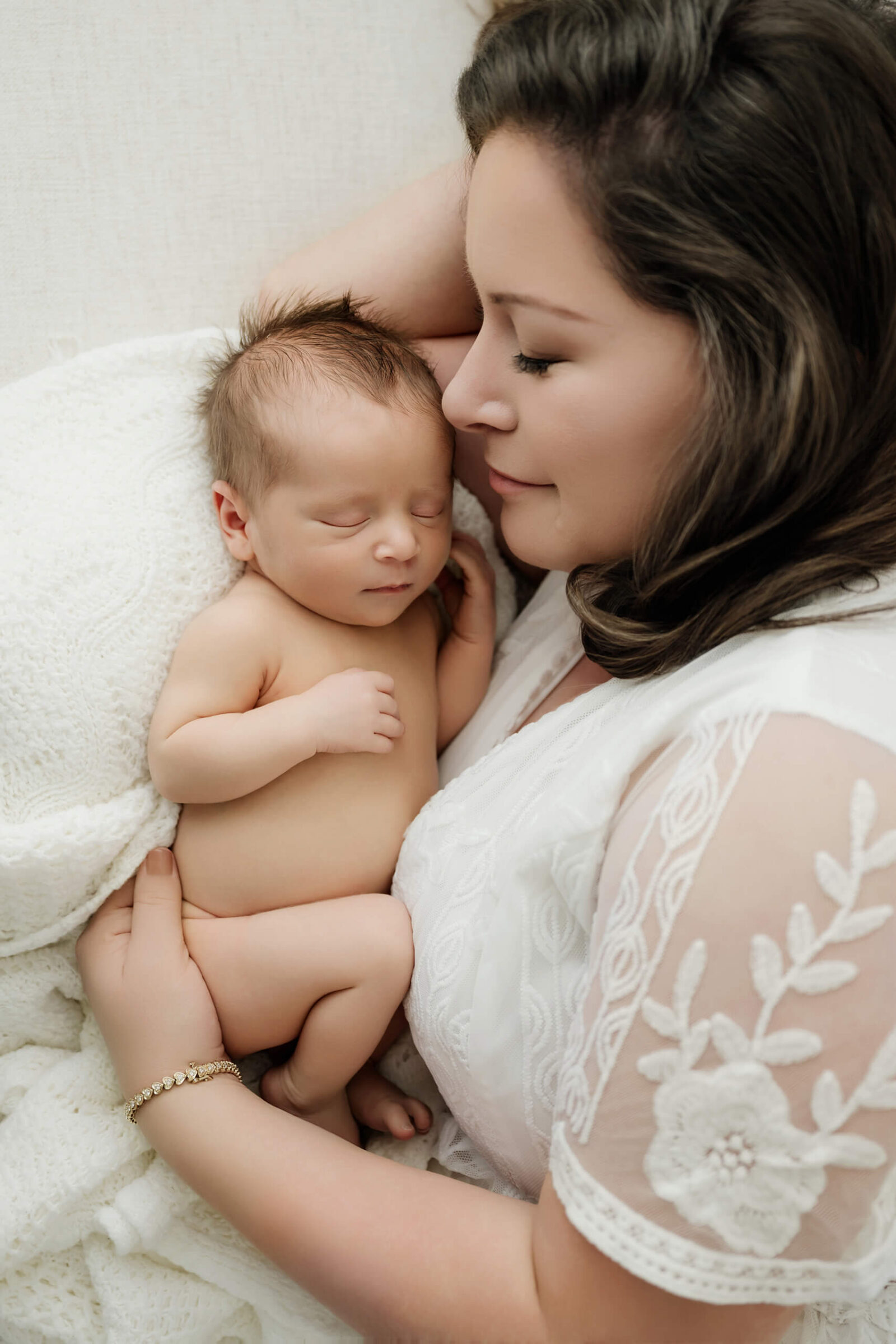 Mom cuddling her sleeping newborn baby during a soft studio newborn session for a maternity and newborn photography package.