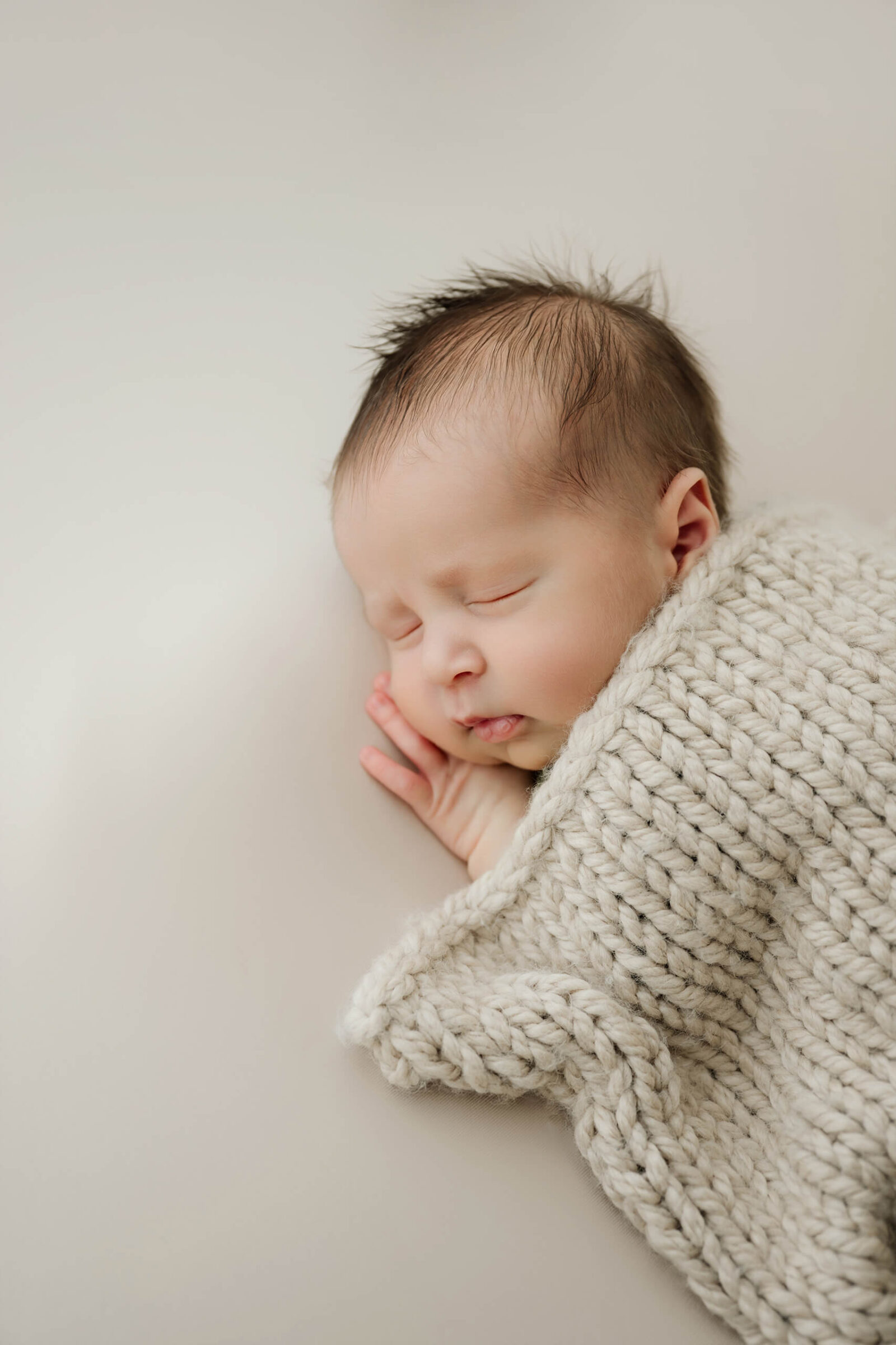 Sleeping newborn baby wrapped in a cream knit blanket during a studio newborn session.