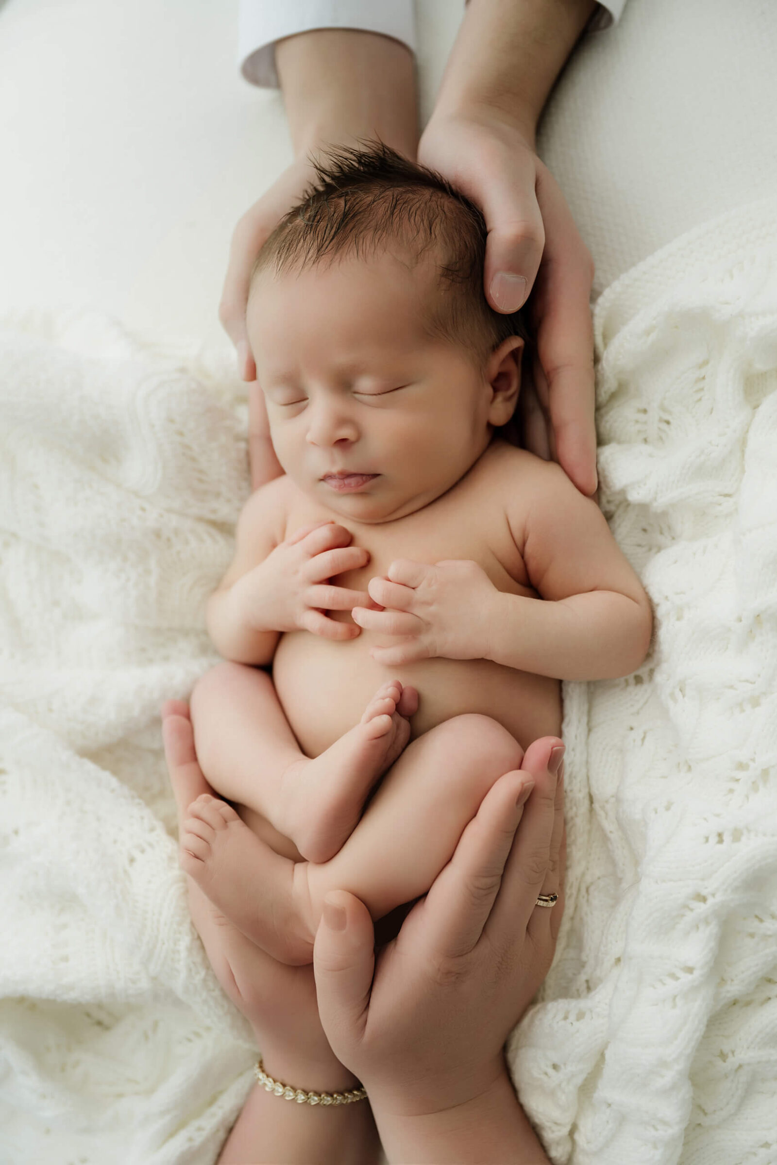 Sleeping newborn baby gently cradled in parents’ hands during a soft studio newborn session.