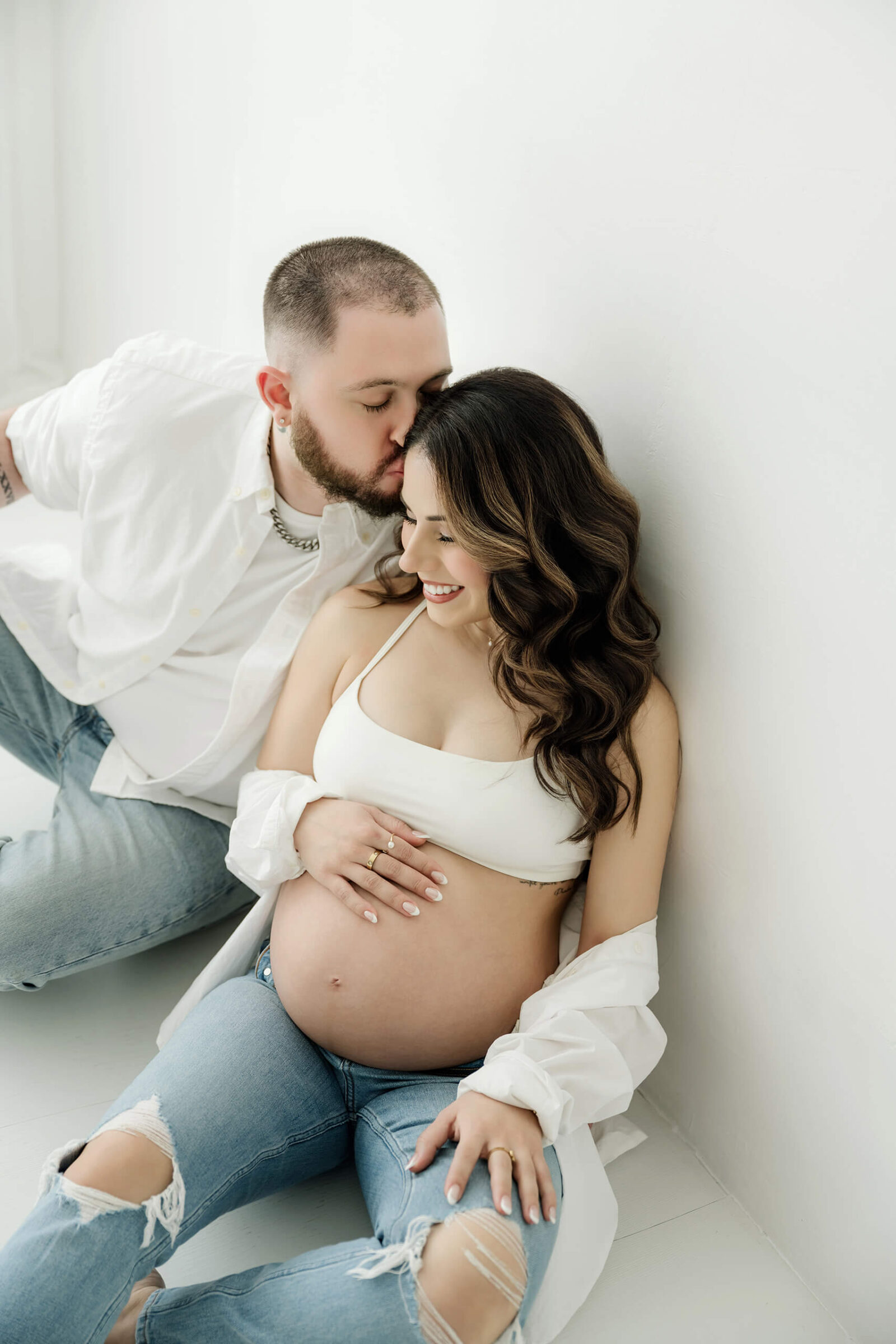 Partner kissing an expecting mom on the forehead during a soft studio maternity session.