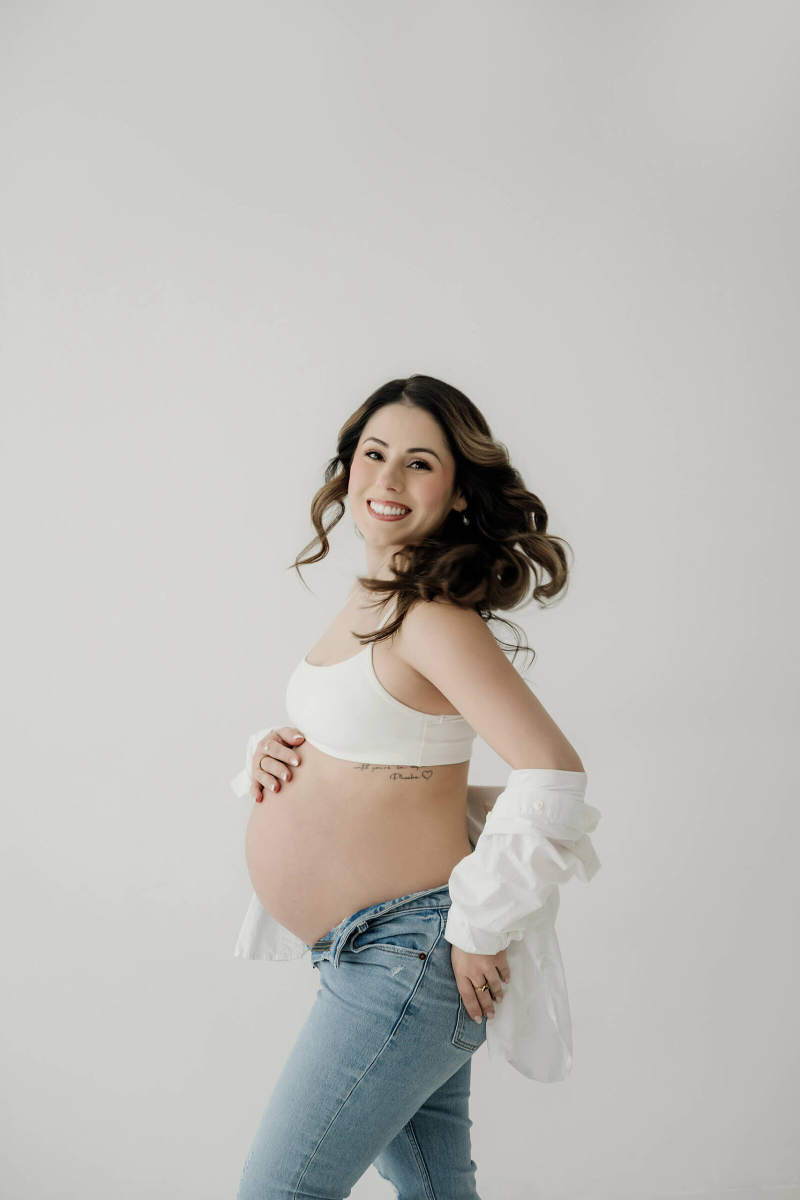 Expecting mom smiling and holding her baby bump during a natural studio maternity portrait.