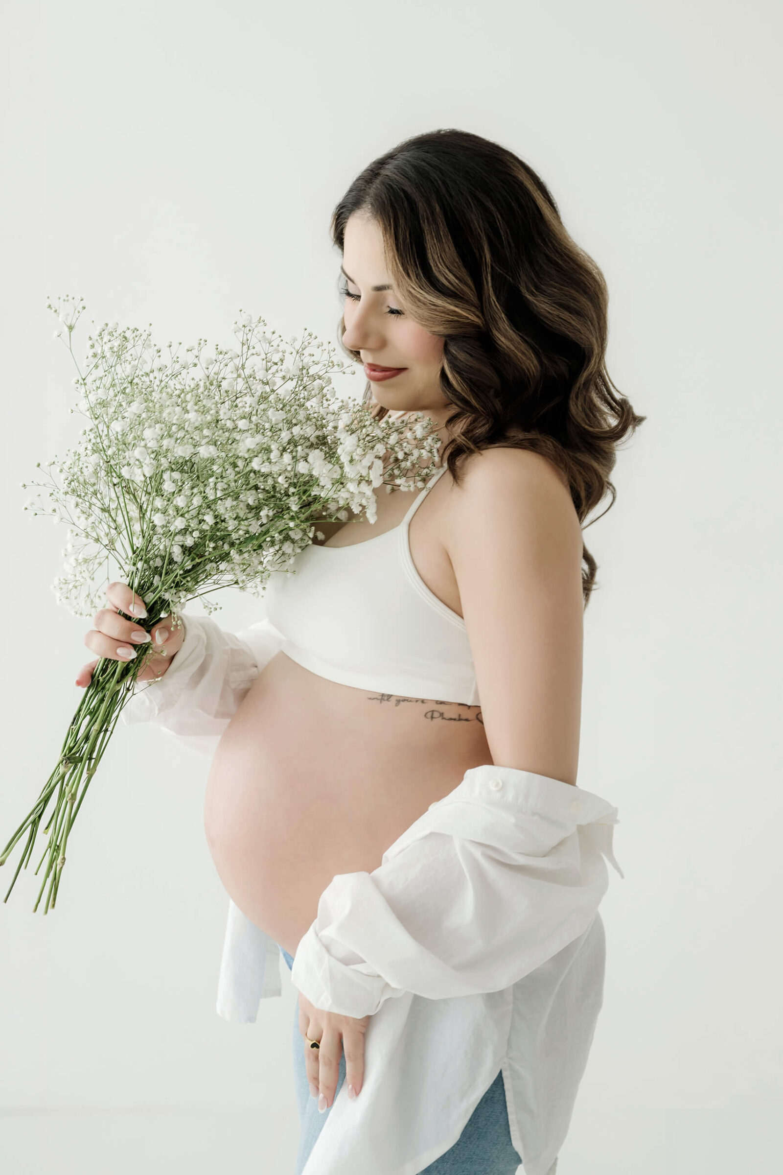 Expecting mom holding white flowers during a simple, light-filled studio maternity session.