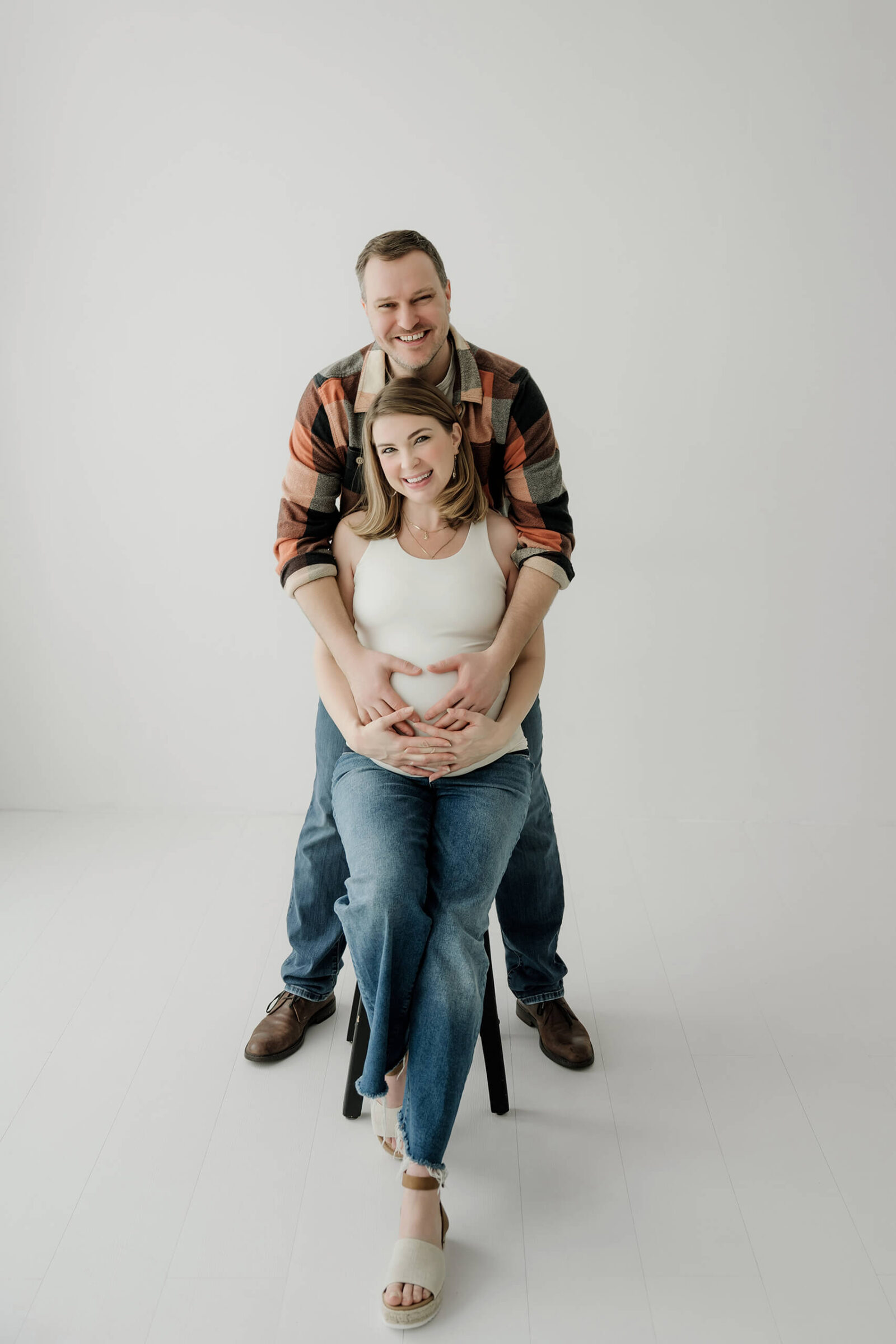 Expecting parents smiling together in a clean white studio during a relaxed maternity session.
