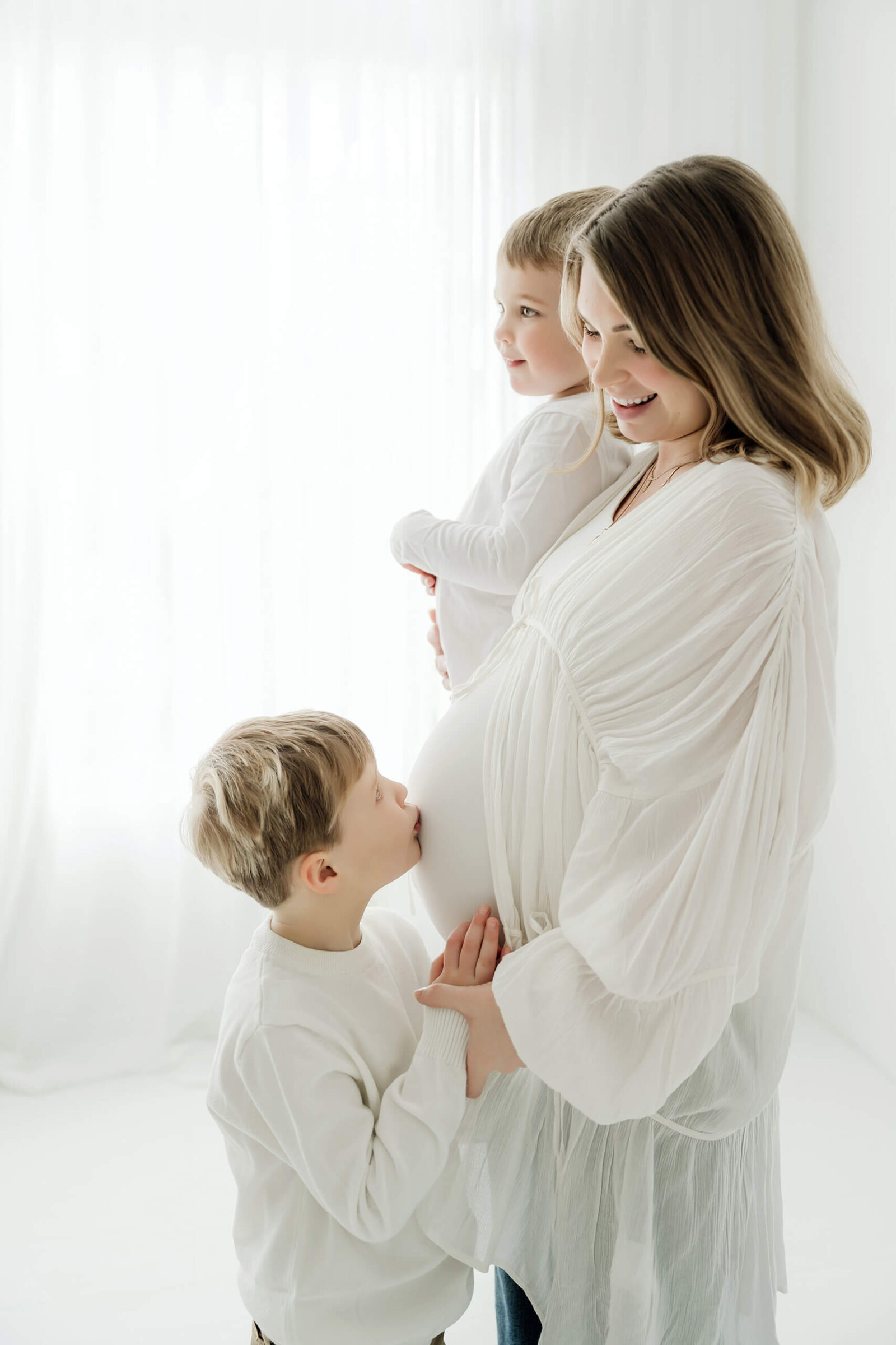 Expecting mom sharing a sweet moment with her two children during a bright studio maternity session.