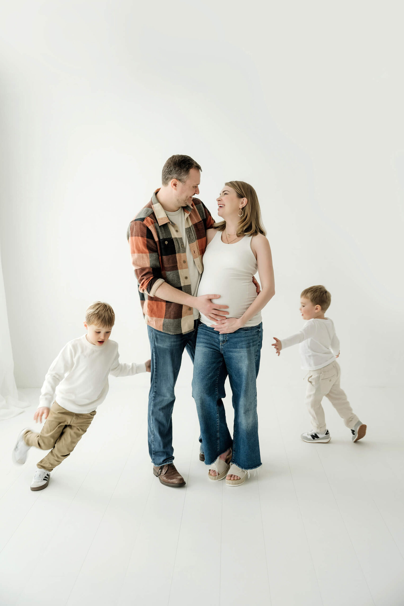 Growing family with two children during a playful white studio maternity session.