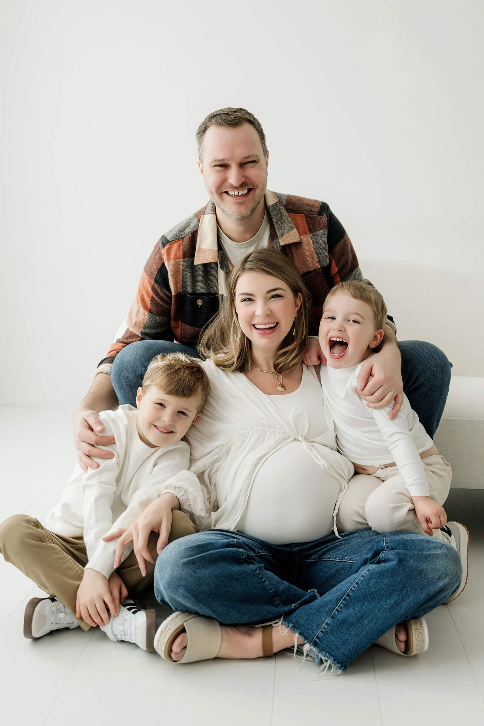 Expecting parents cuddling with their two children during a relaxed studio maternity session.