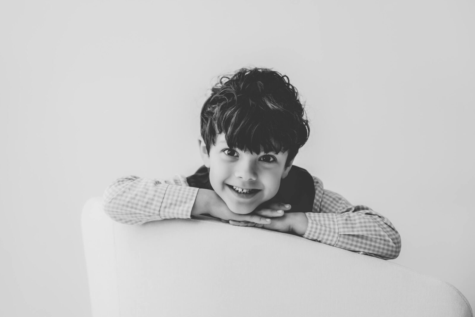 Smiling young boy leaning over a chair during a black-and-white family photography studio portrait near Bellevue.