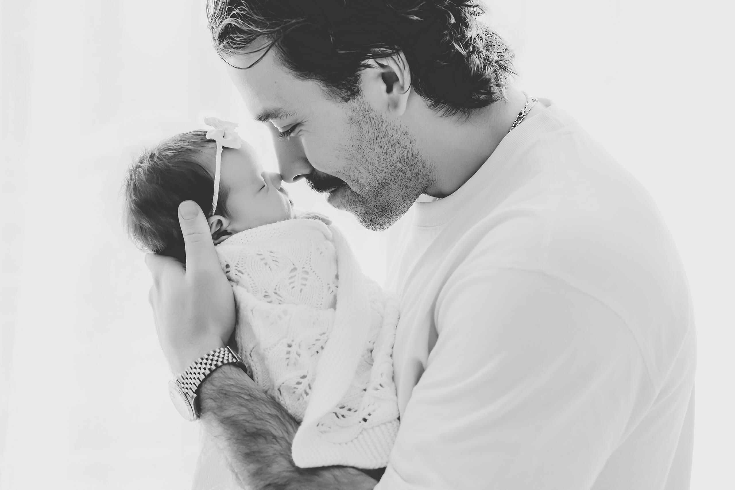 Father holding his newborn daughter close during a black-and-white newborn portrait session.