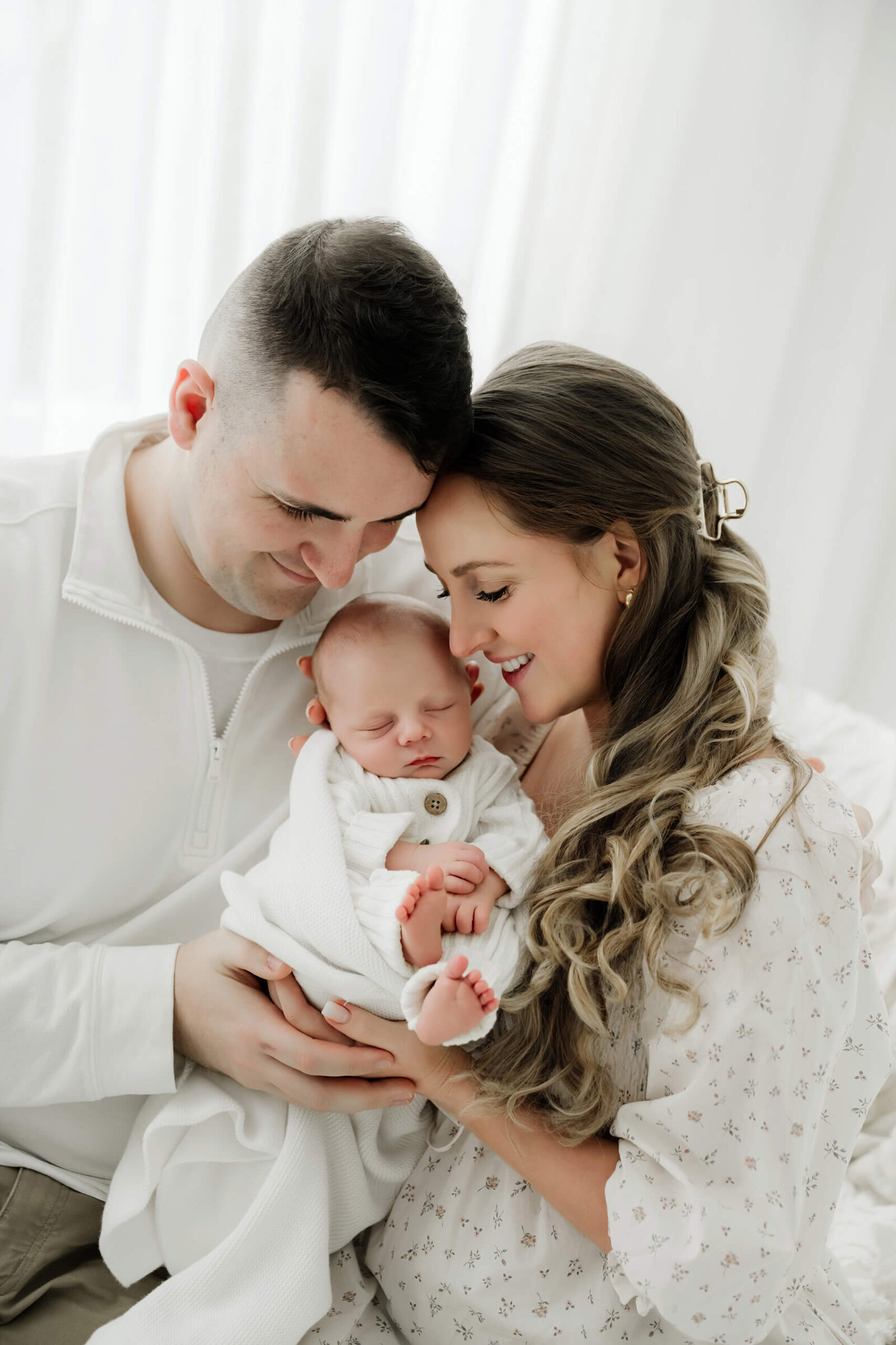 Parents cuddling their sleeping newborn during a soft, white studio newborn portrait session.
