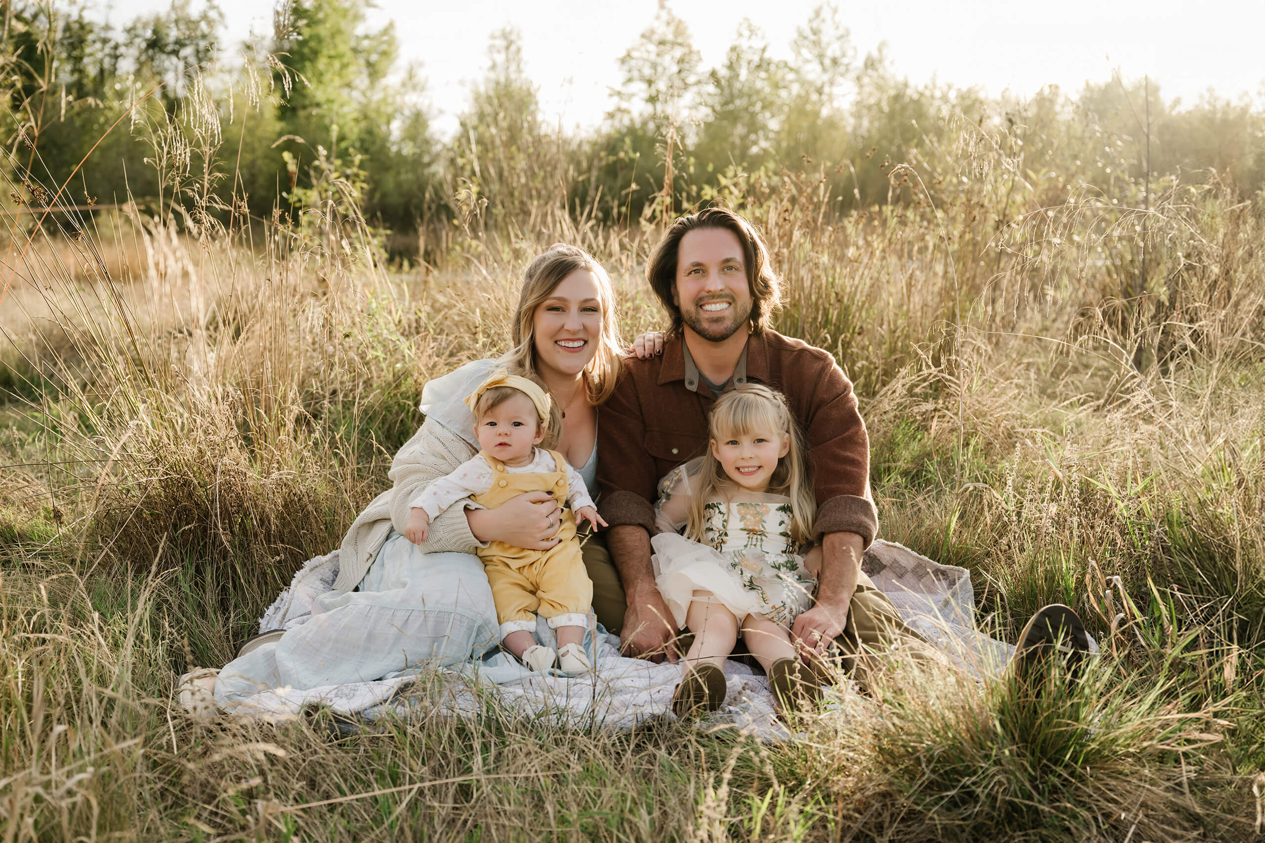 Family of four sitting together in tall grass during an outdoor Kirkland family photography session.