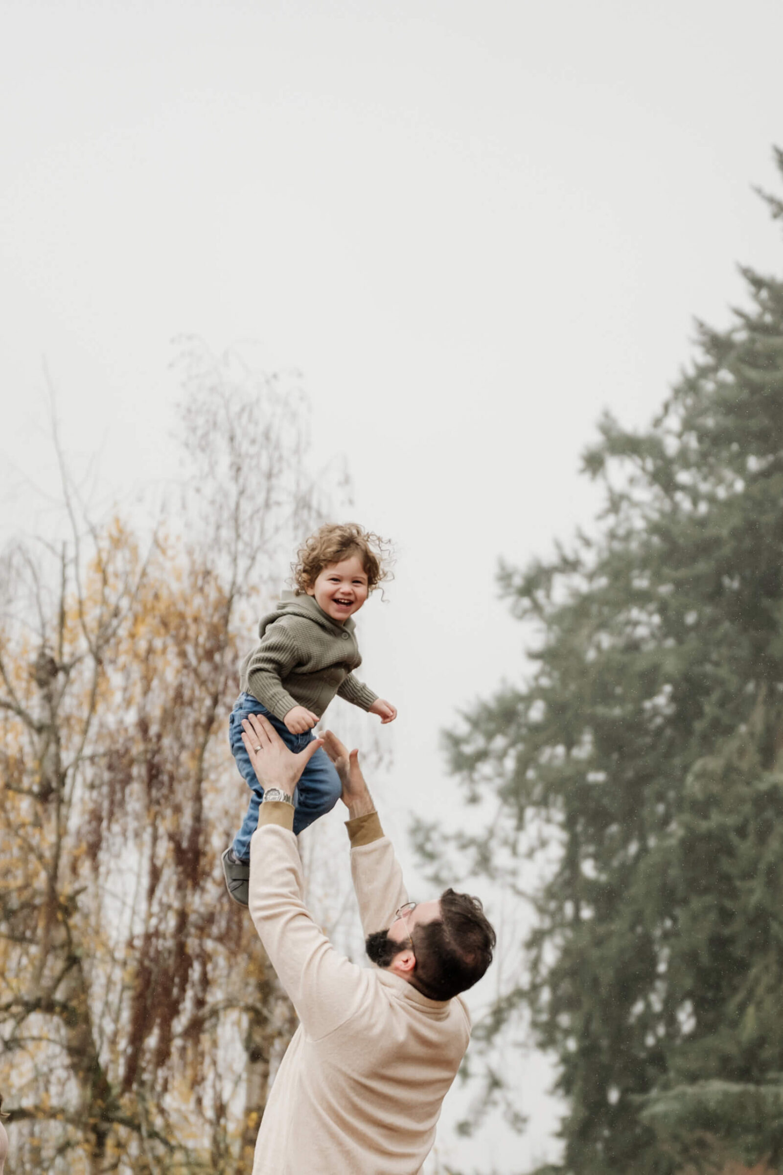 Father lifting his laughing toddler during a Kirkland outdoor family photography session in fall.