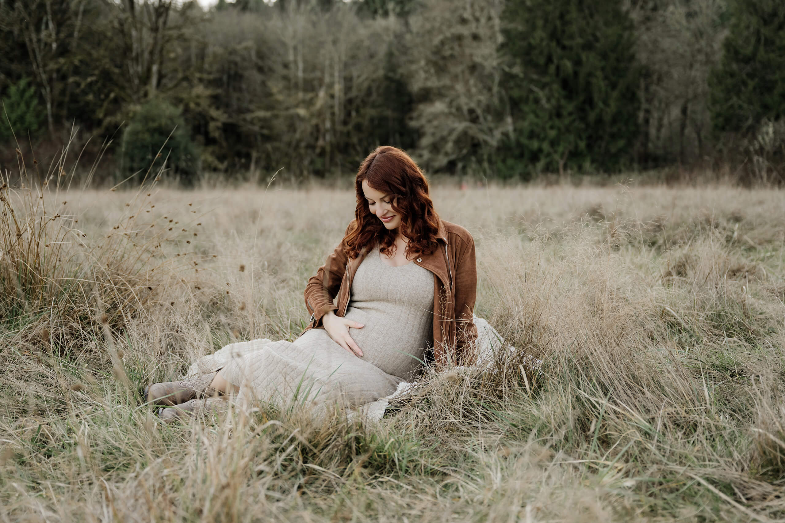 Pregnant mother sitting in tall grass during a natural Kirkland maternity photography session.