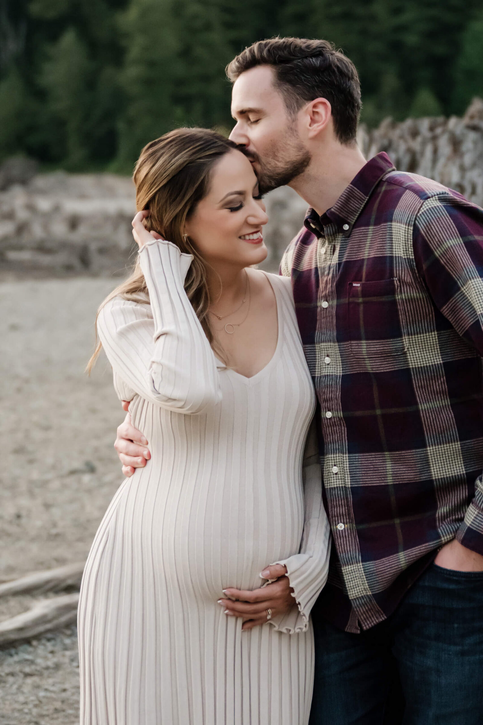 Partner kissing pregnant mother’s forehead during a close outdoor maternity portrait.