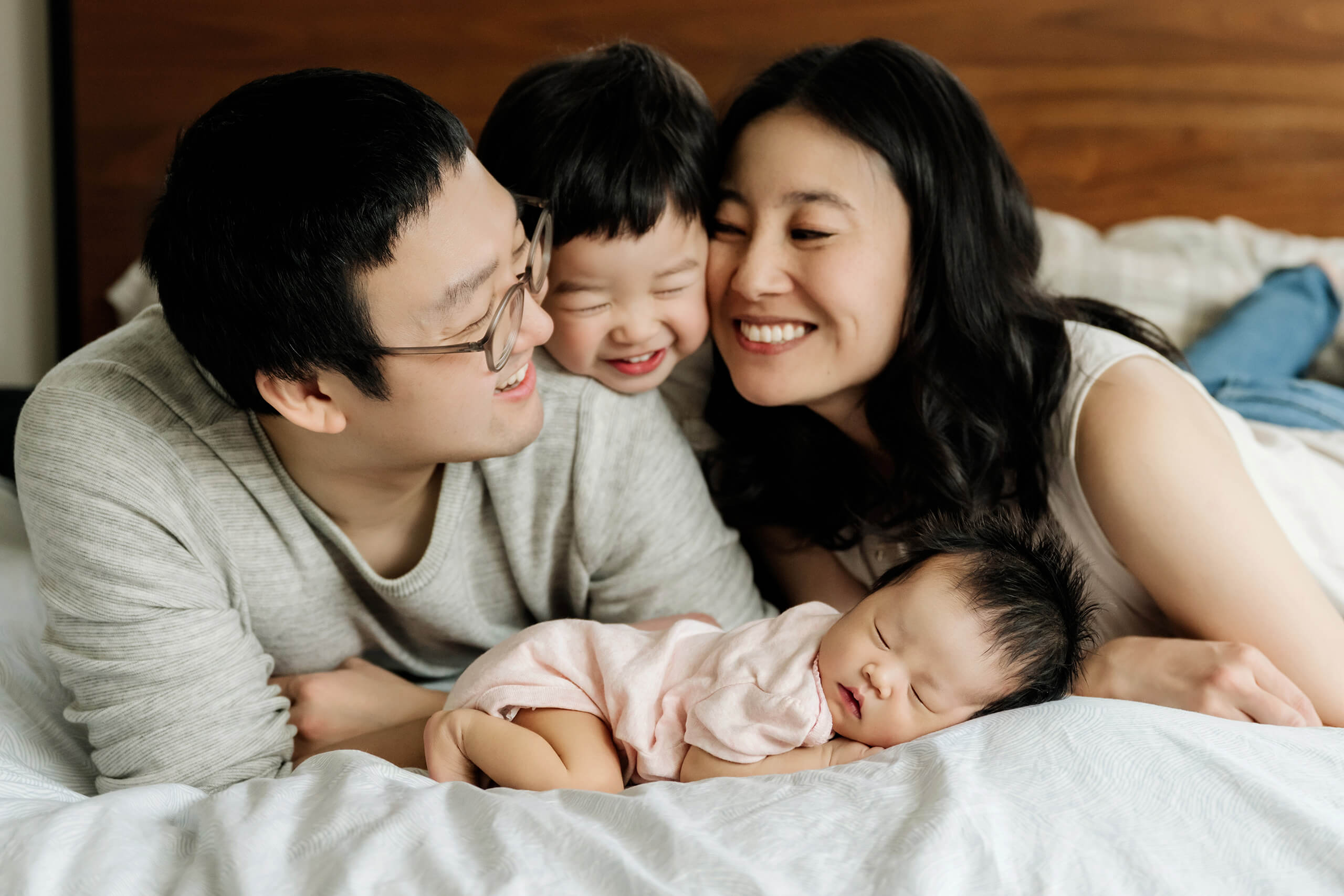 Family gathered on a bed with a sleeping newborn during a relaxed Kirkland newborn photography session.