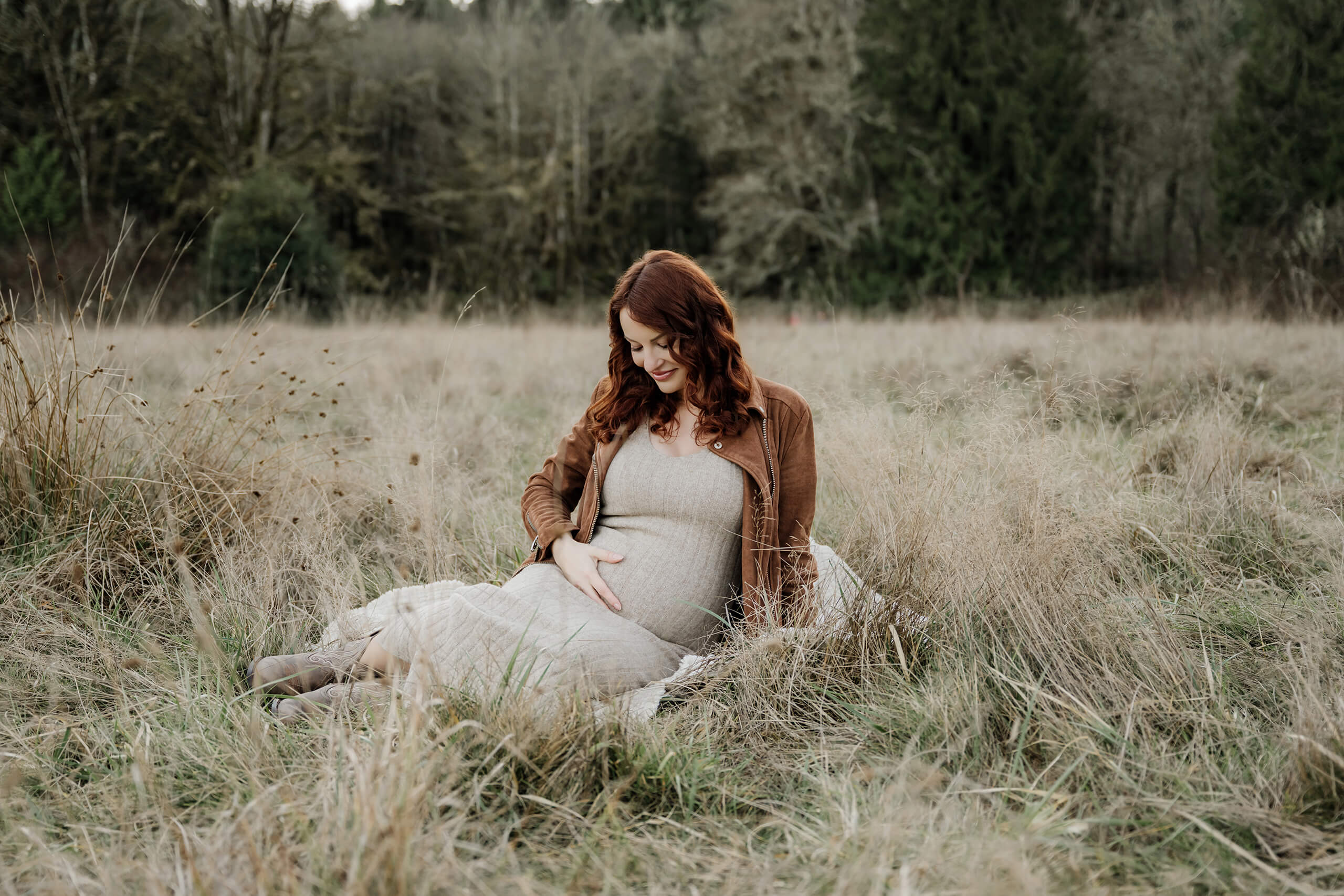 Pregnant mother sitting in tall grass during a natural outdoor maternity photo session.