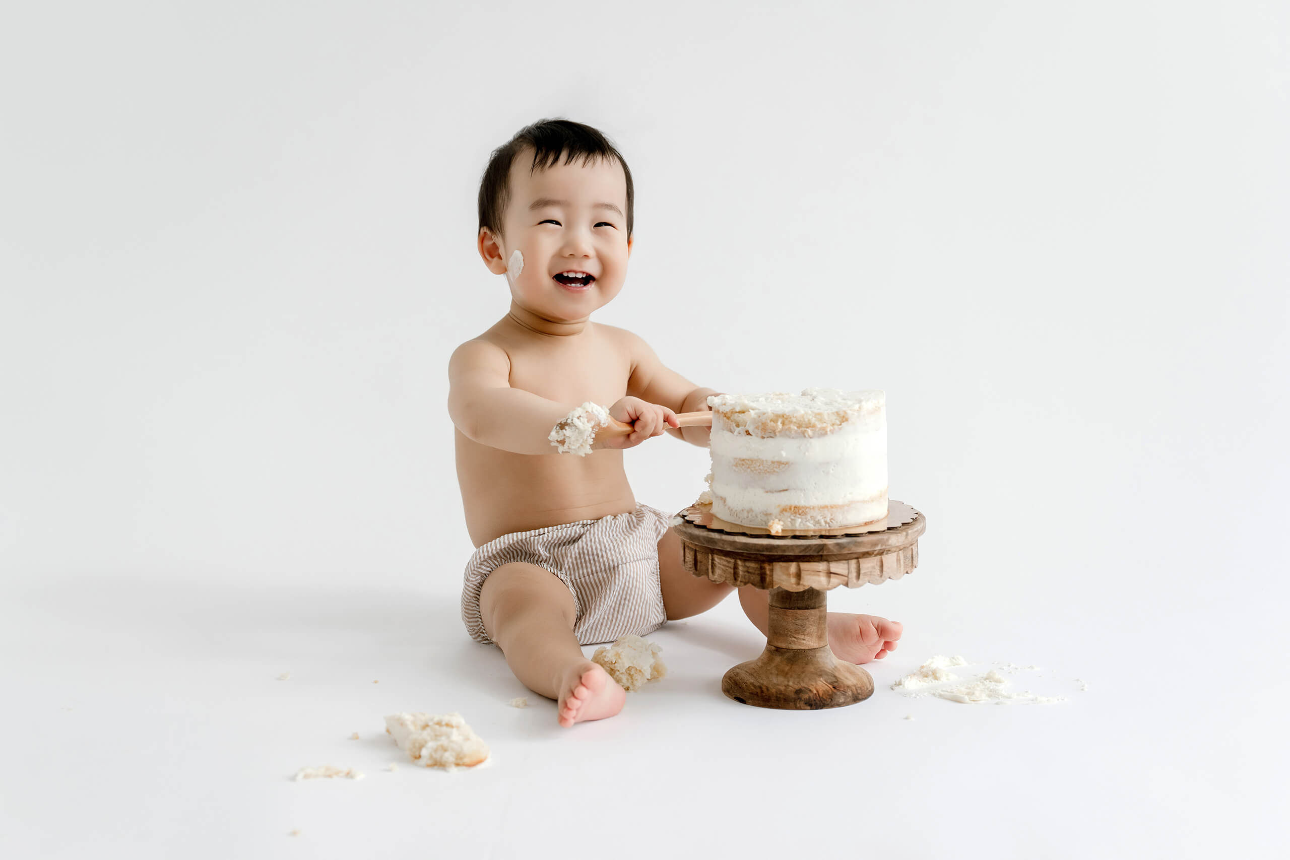 Smiling baby playing with a white birthday cake during a Mercer Island cake smash photography session.