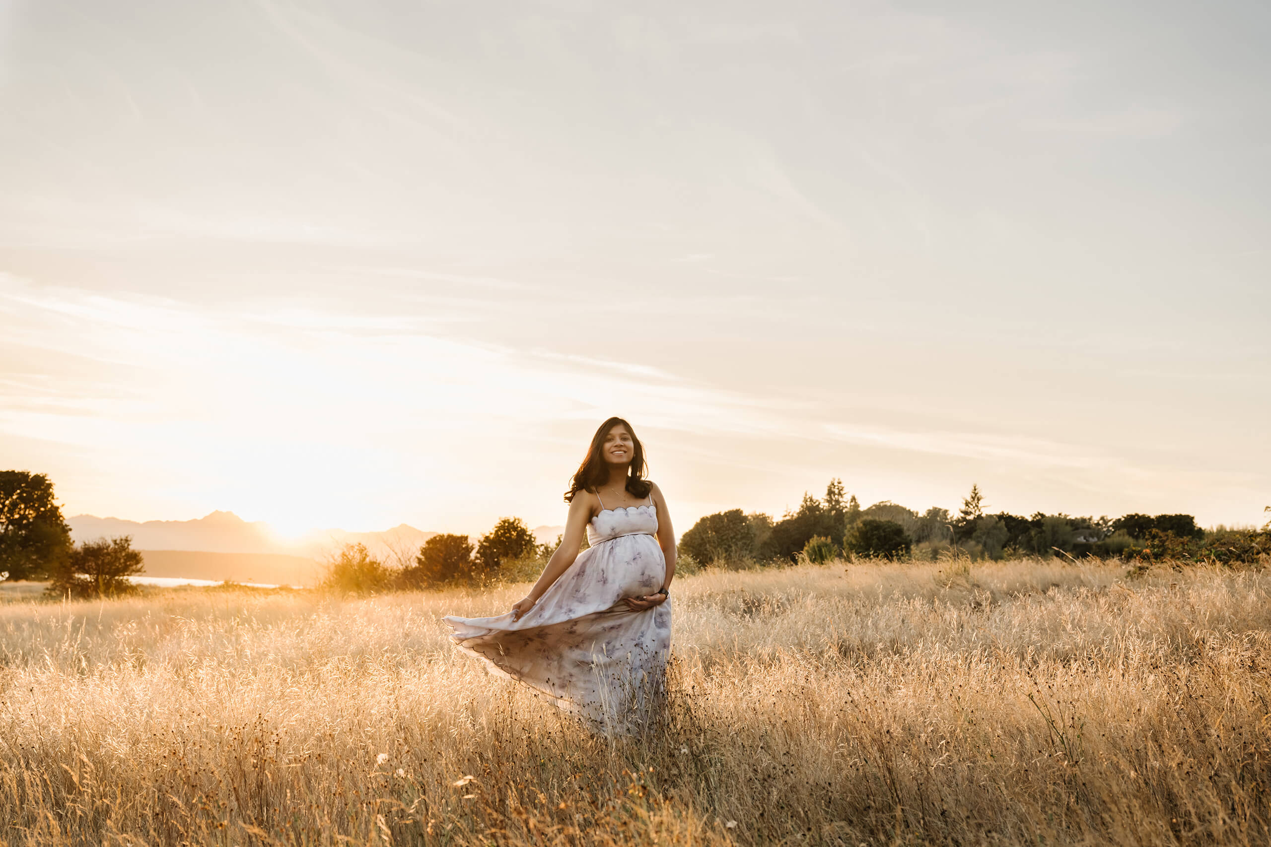 Pregnant mother standing in a golden field at sunset during an outdoor maternity photo session.