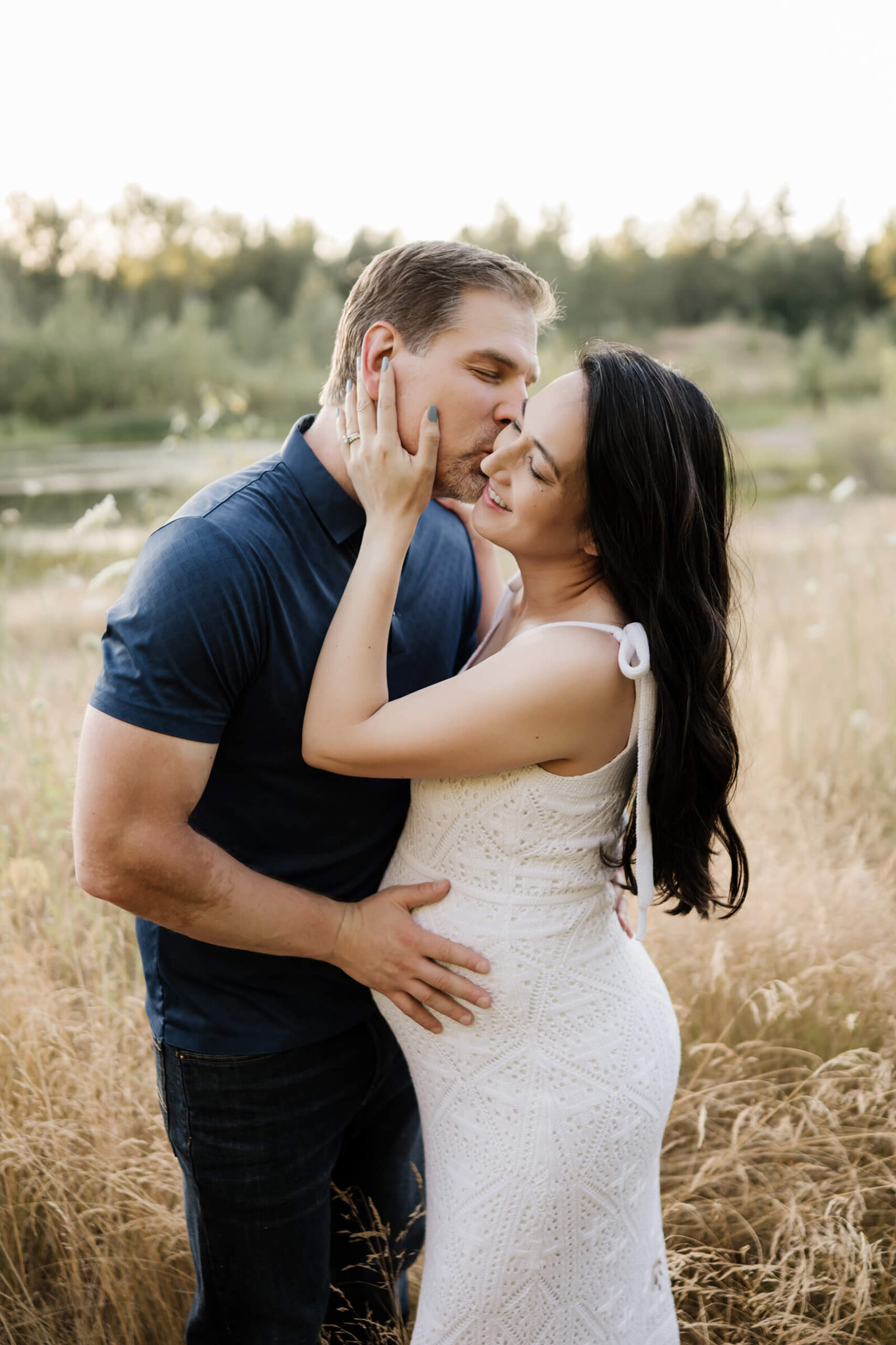 Expecting couple embracing in a grassy field during a natural outdoor maternity portrait.