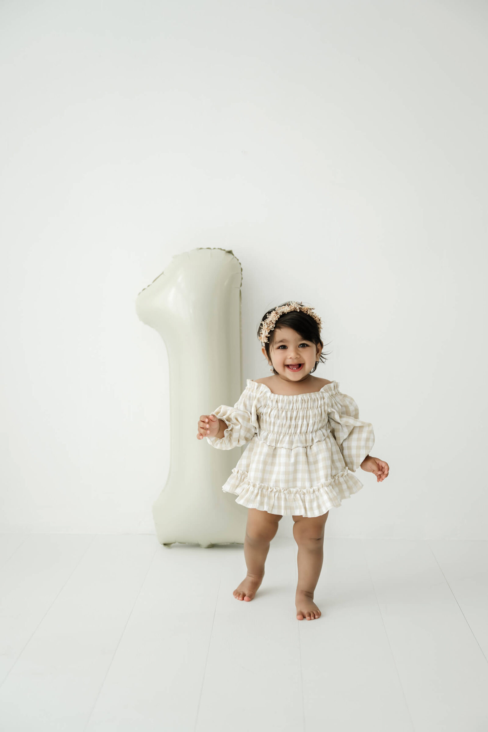 Smiling one-year-old standing next to a large number one balloon during a Redmond milestone photography session.