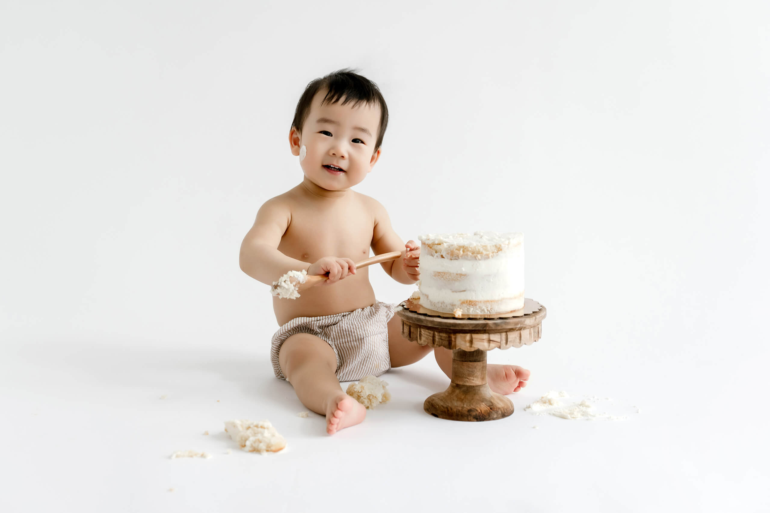 One-year-old laughing beside a white birthday cake during a Sammamish milestone photography session.