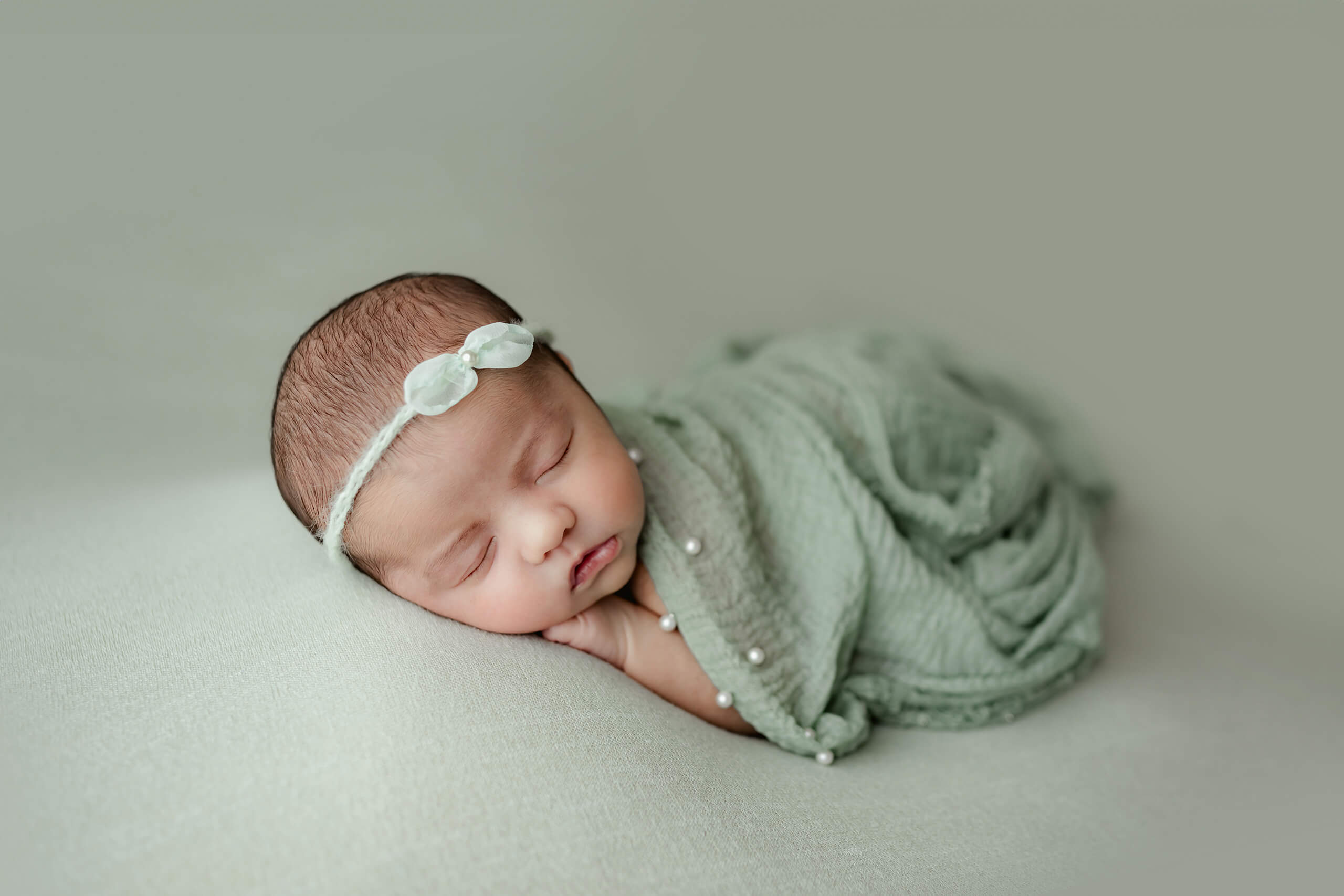 Sleeping newborn wrapped in soft green fabric during a simple studio newborn portrait.