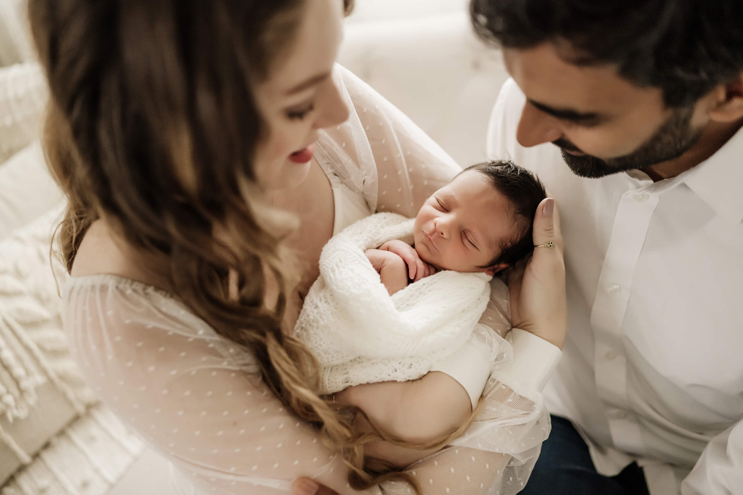 Parents holding their sleeping newborn close during a soft studio newborn portrait.