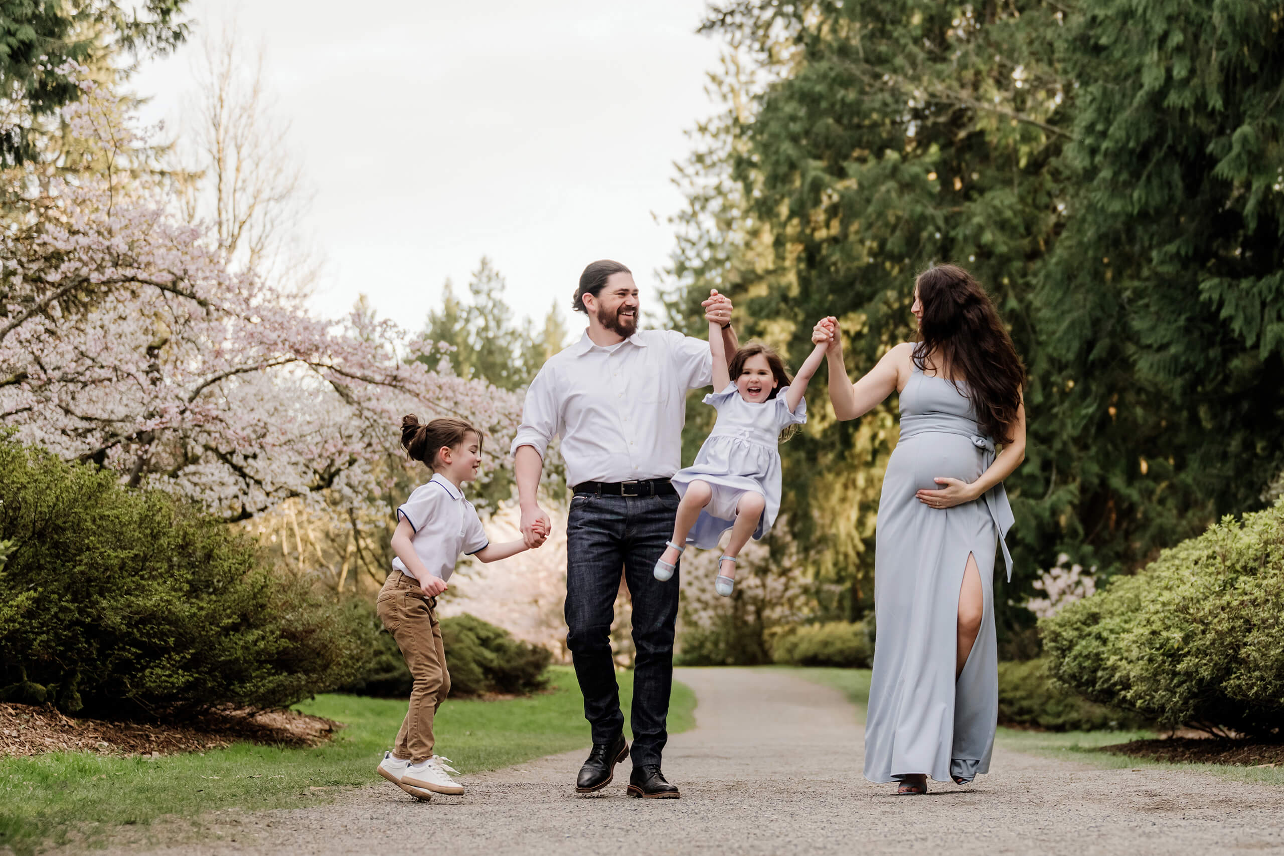 Pregnant mom walking with her family under spring blossoms during an outdoor maternity and family session.