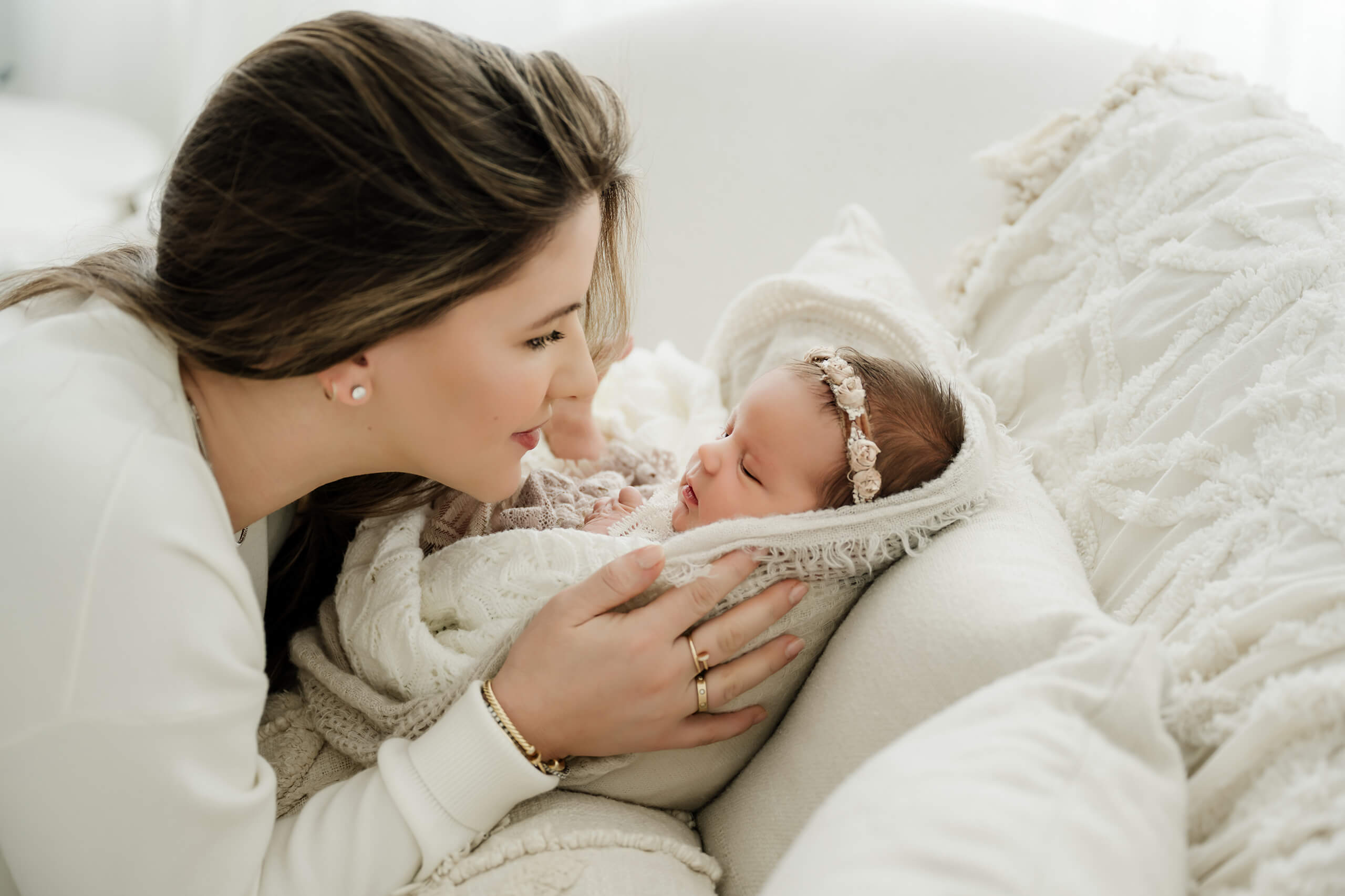 Mother smiling at her wrapped newborn during a soft, neutral studio newborn photography session.