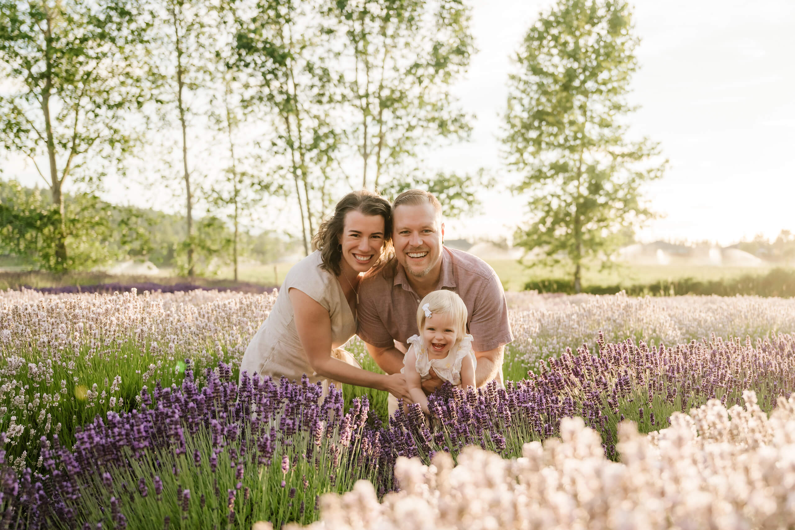 Parents smiling with their young daughter in a lavender field during an outdoor family session.
