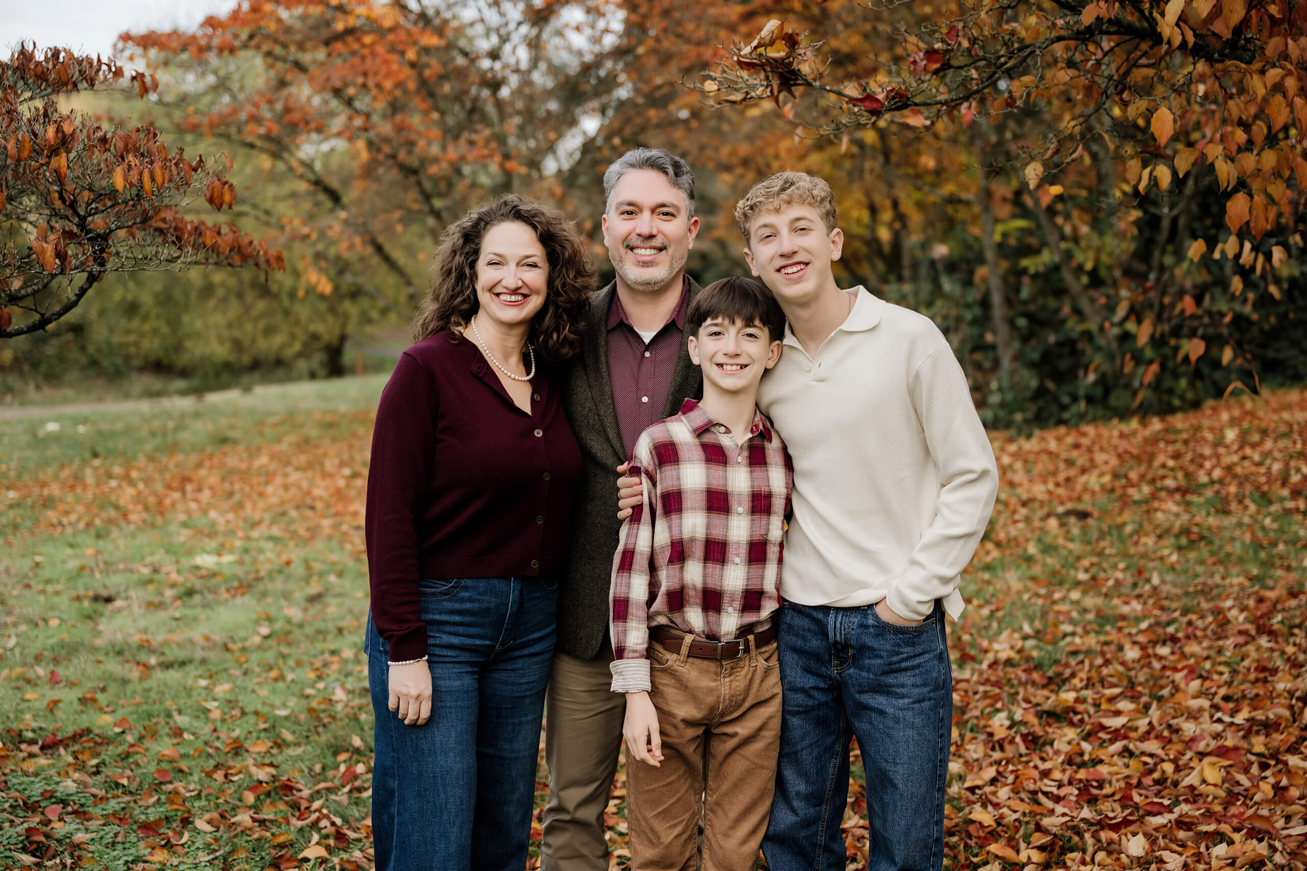 Family of four standing together under fall leaves during outdoor family portraits.