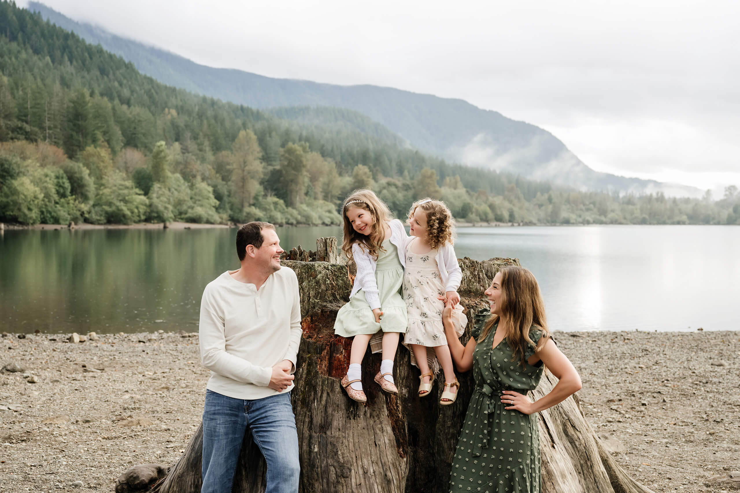 Family of four laughing together by a mountain lake during a Seattle outdoor family session.