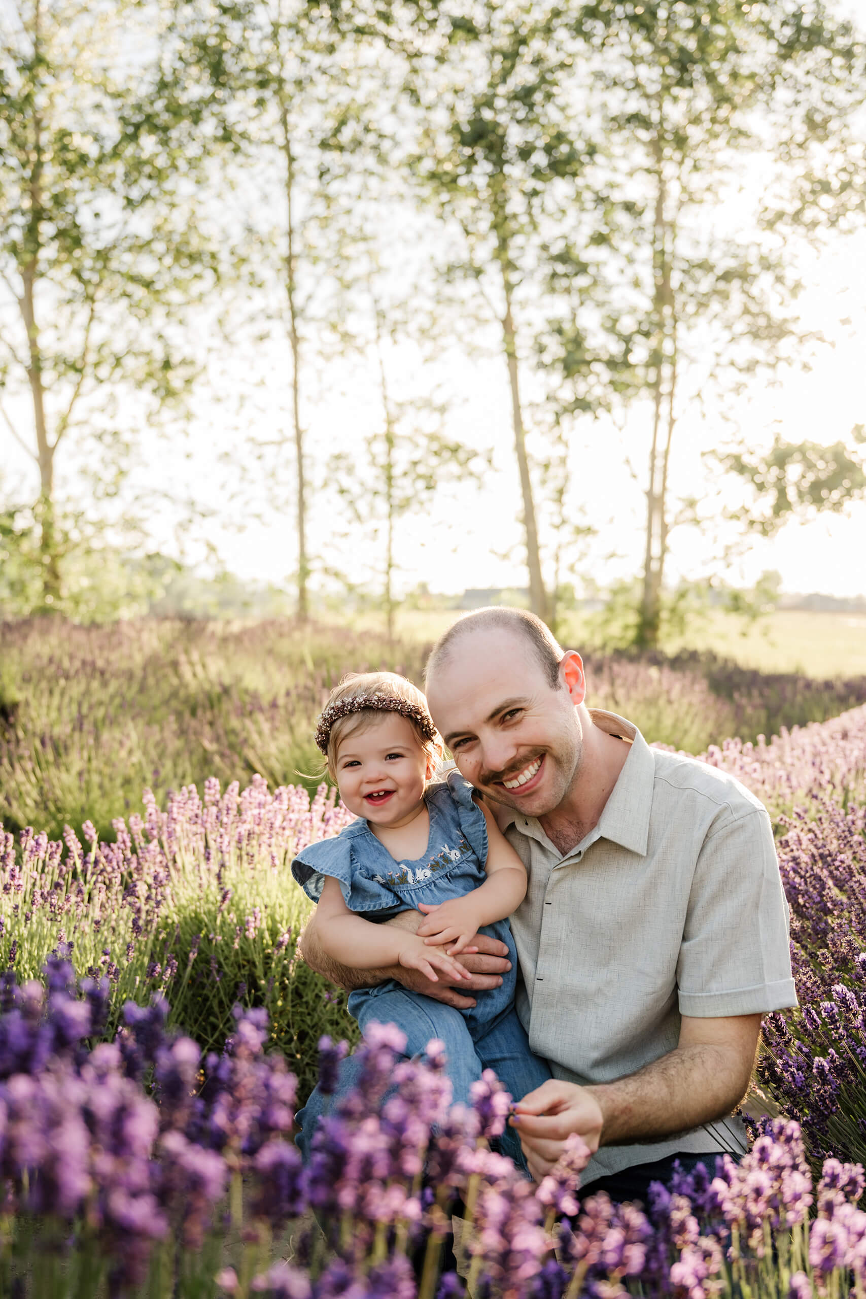 Dad and young daughter sitting together in a lavender field with soft evening light behind them.
