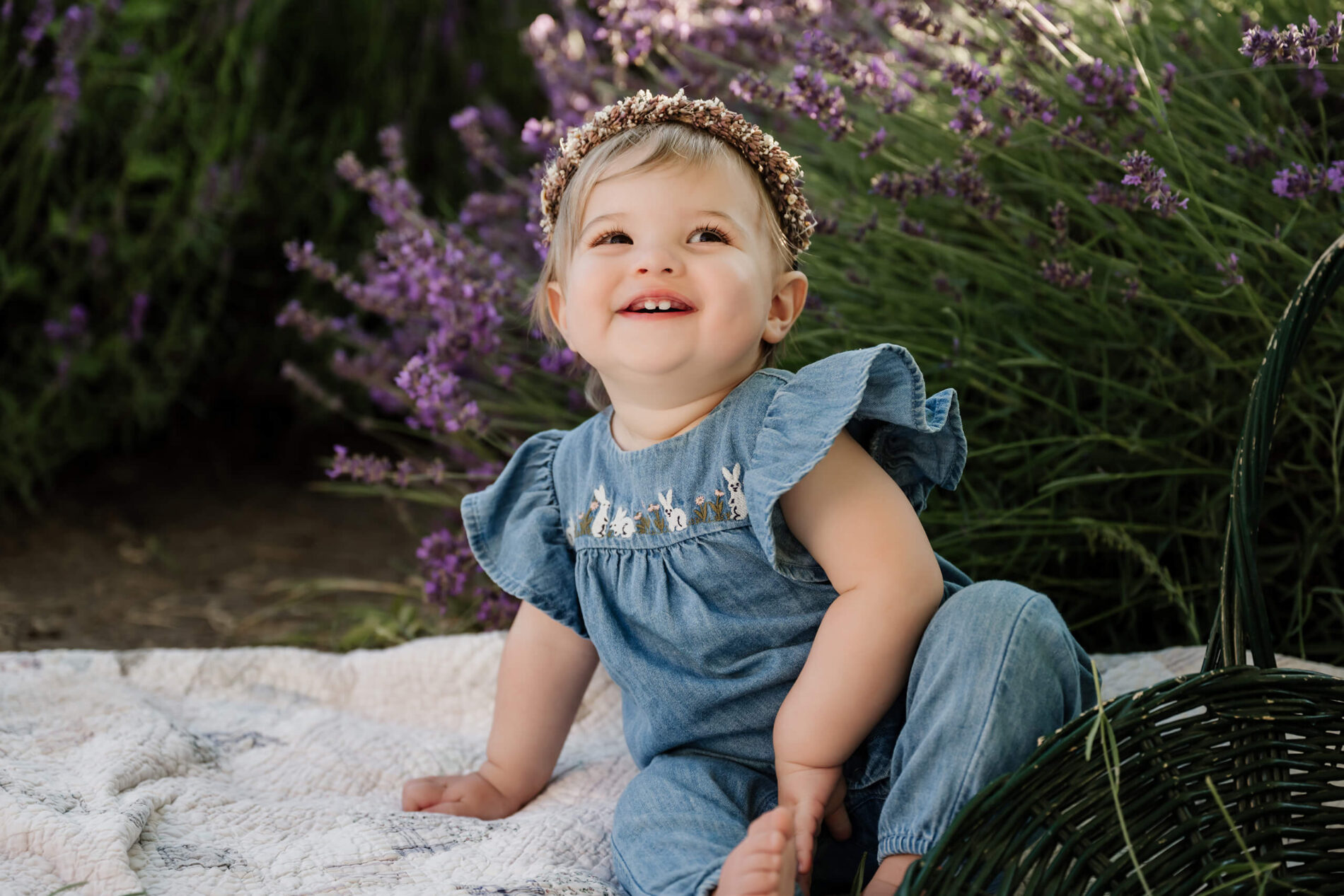 Smiling toddler sitting on a quilt beside lavender blooms during a lavender farm family session.