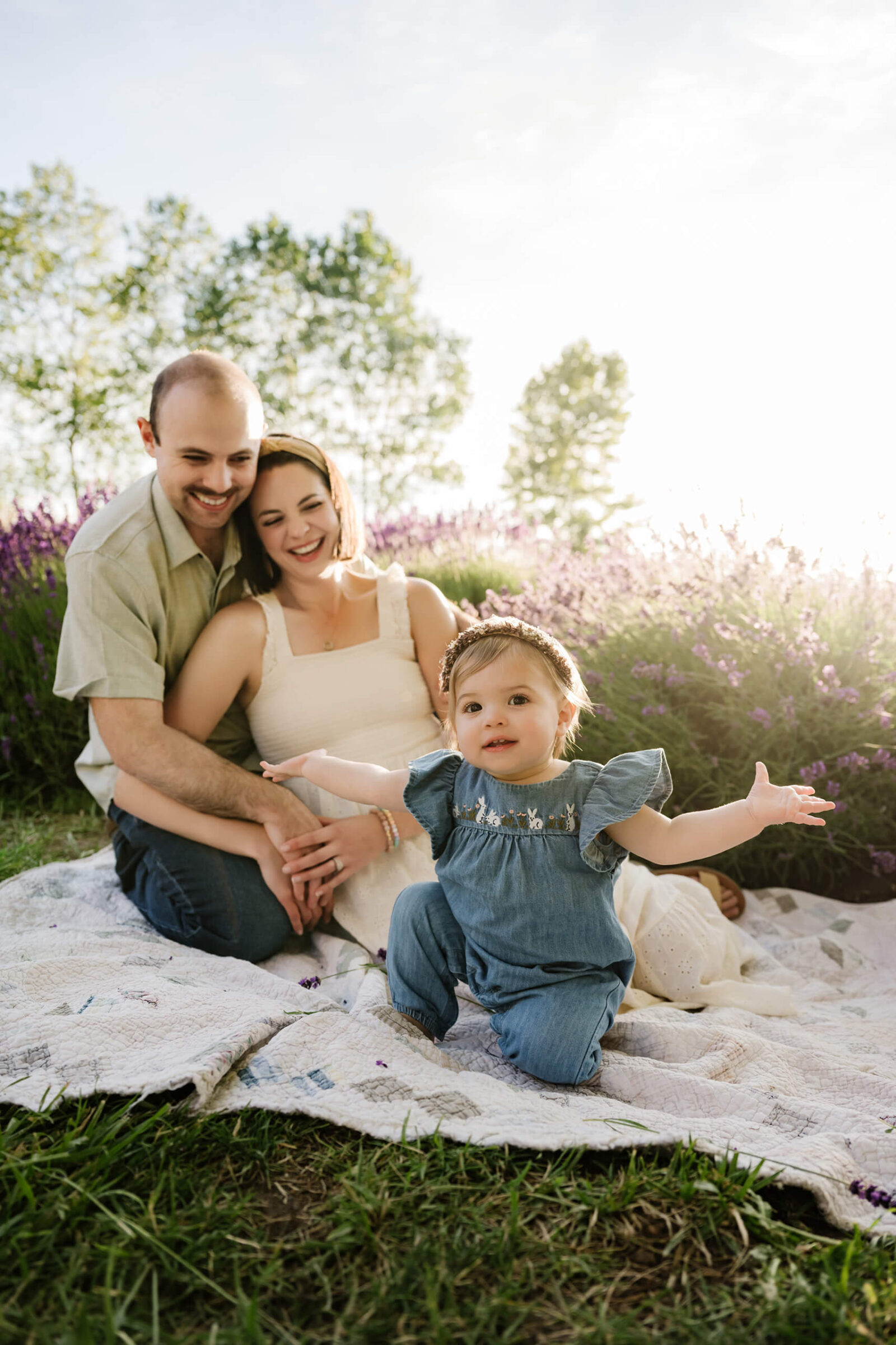 Toddler reaching toward the camera while her parents smile behind her at a Sequim lavender farm.