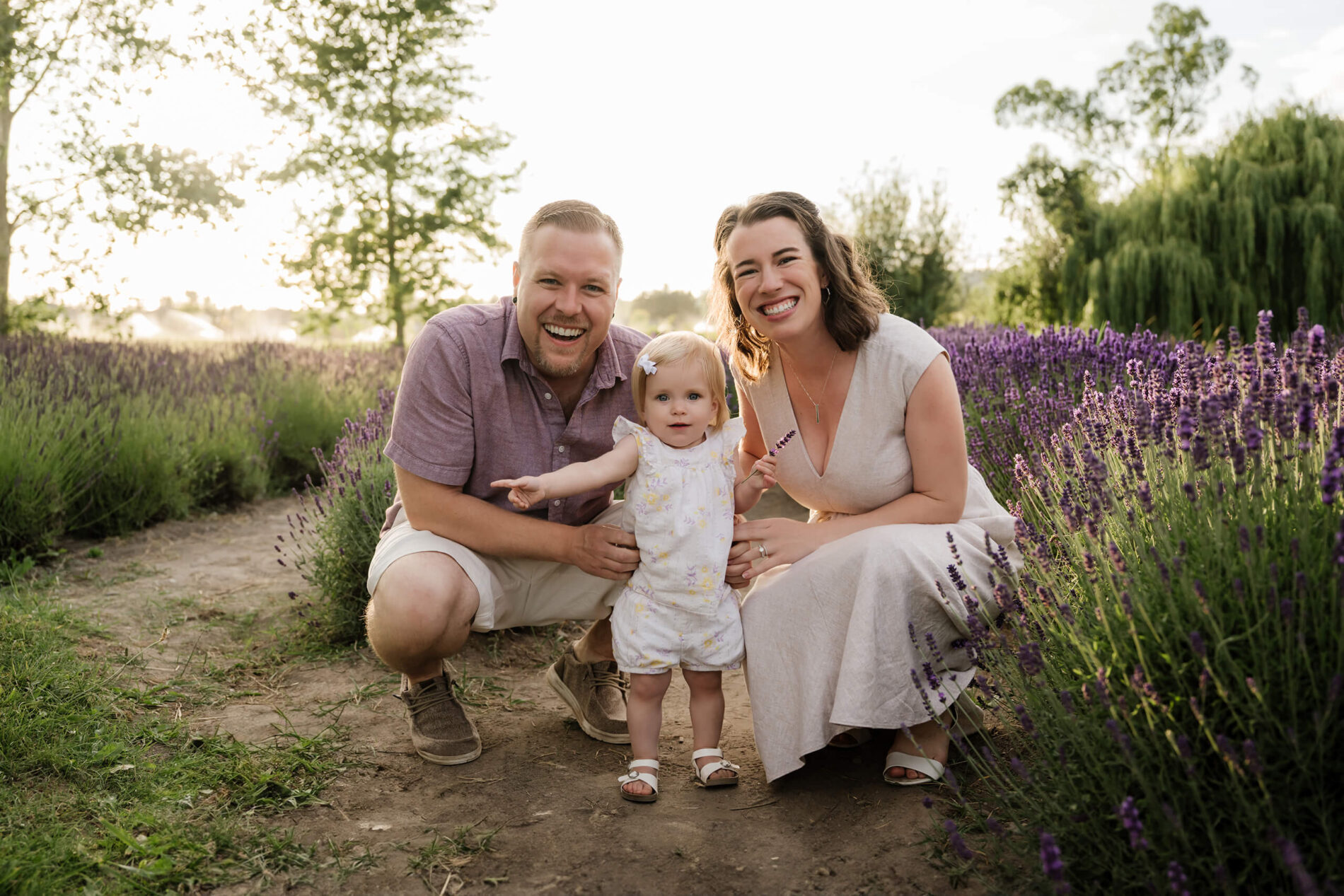 Family of three crouched together between lavender rows during a relaxed outdoor session.