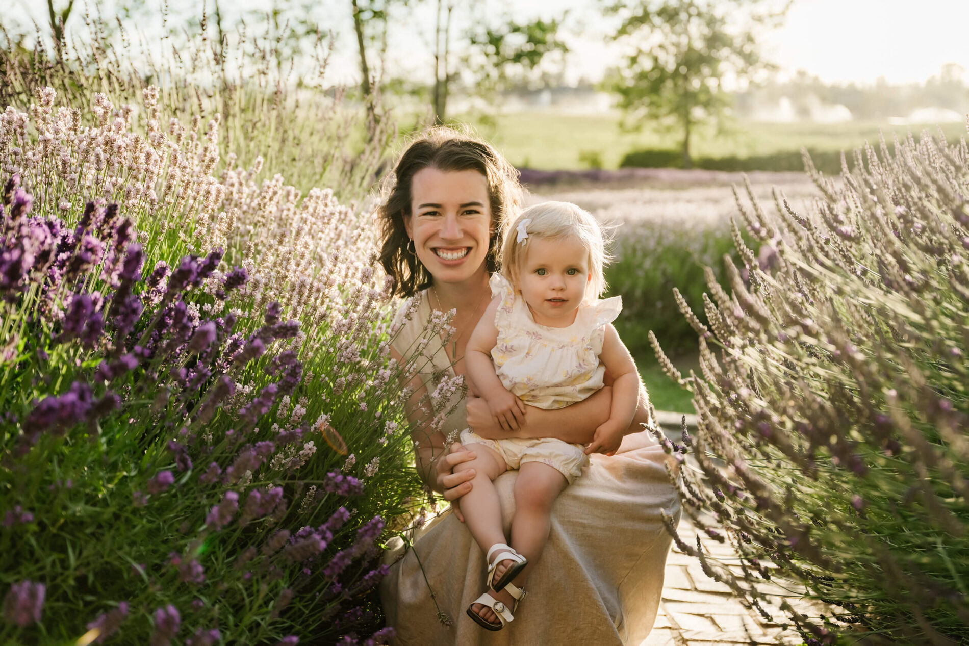 Mom holding her toddler between lavender rows during a soft evening family session.